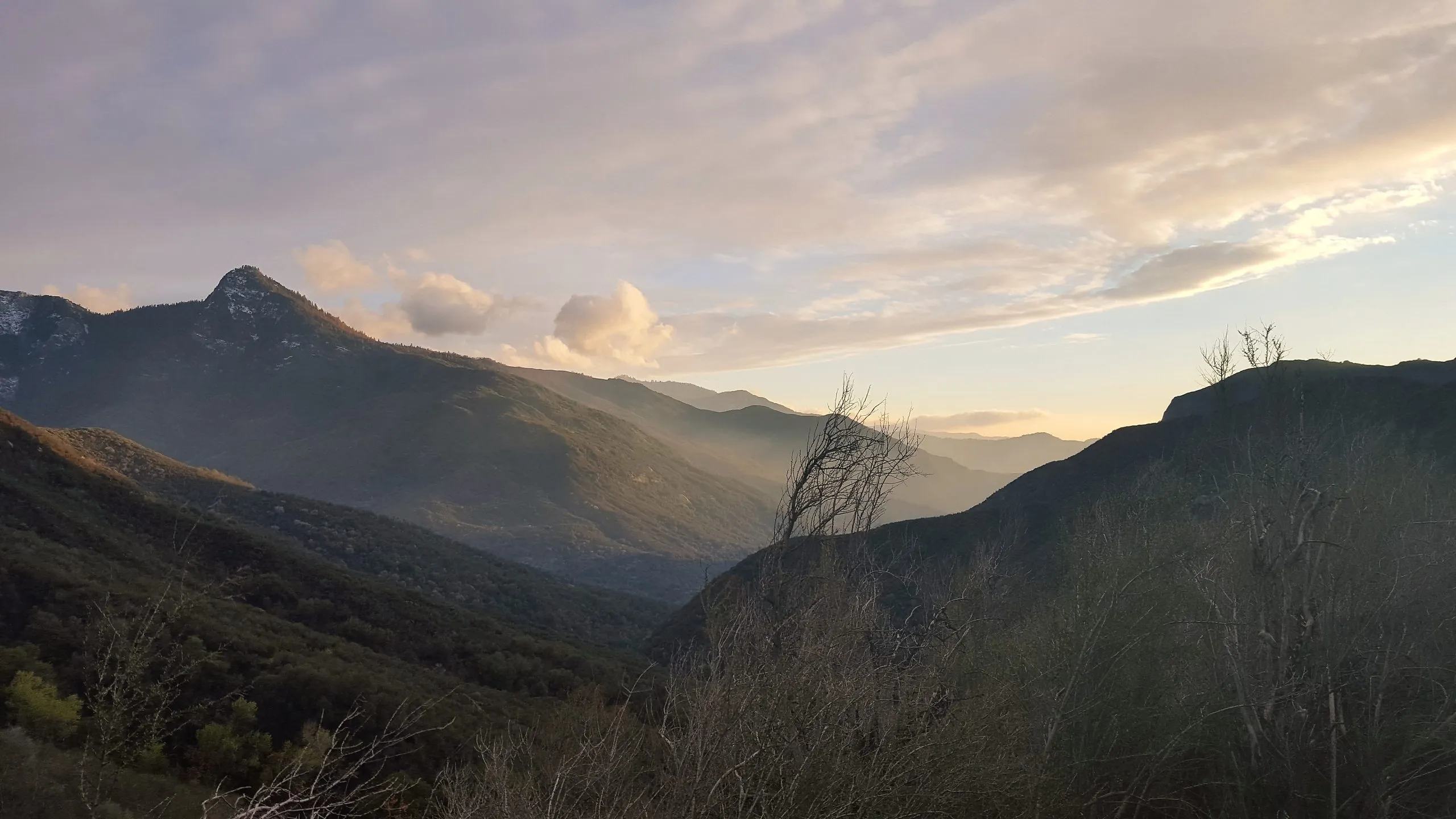 Layered mountain ridges receding into a misty blue valley under a sunset sky with gold and pink clouds, Sequoia National Park.