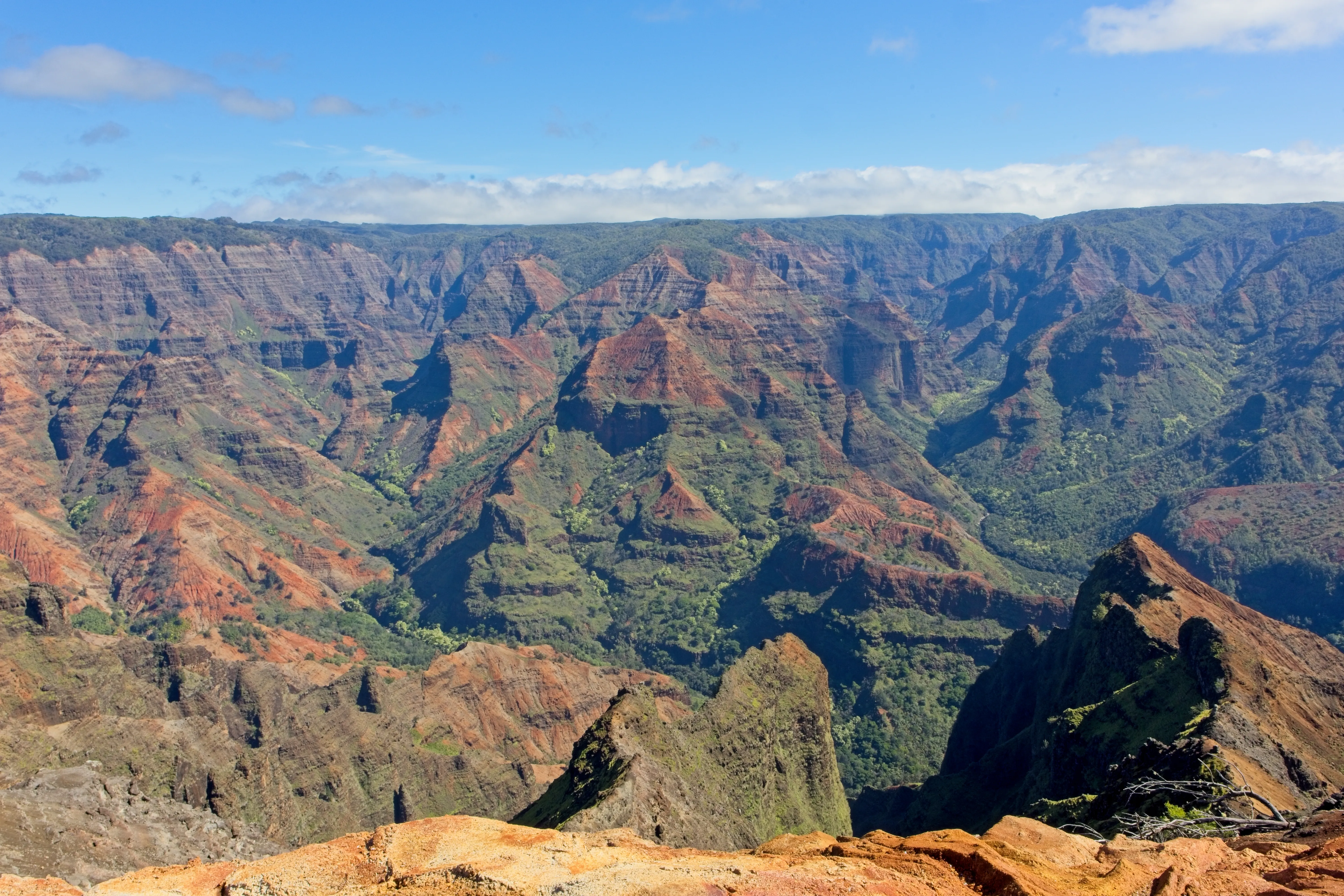 Panoramic view of red and green canyon ridges under blue sky at Waimea Canyon, Kauai.