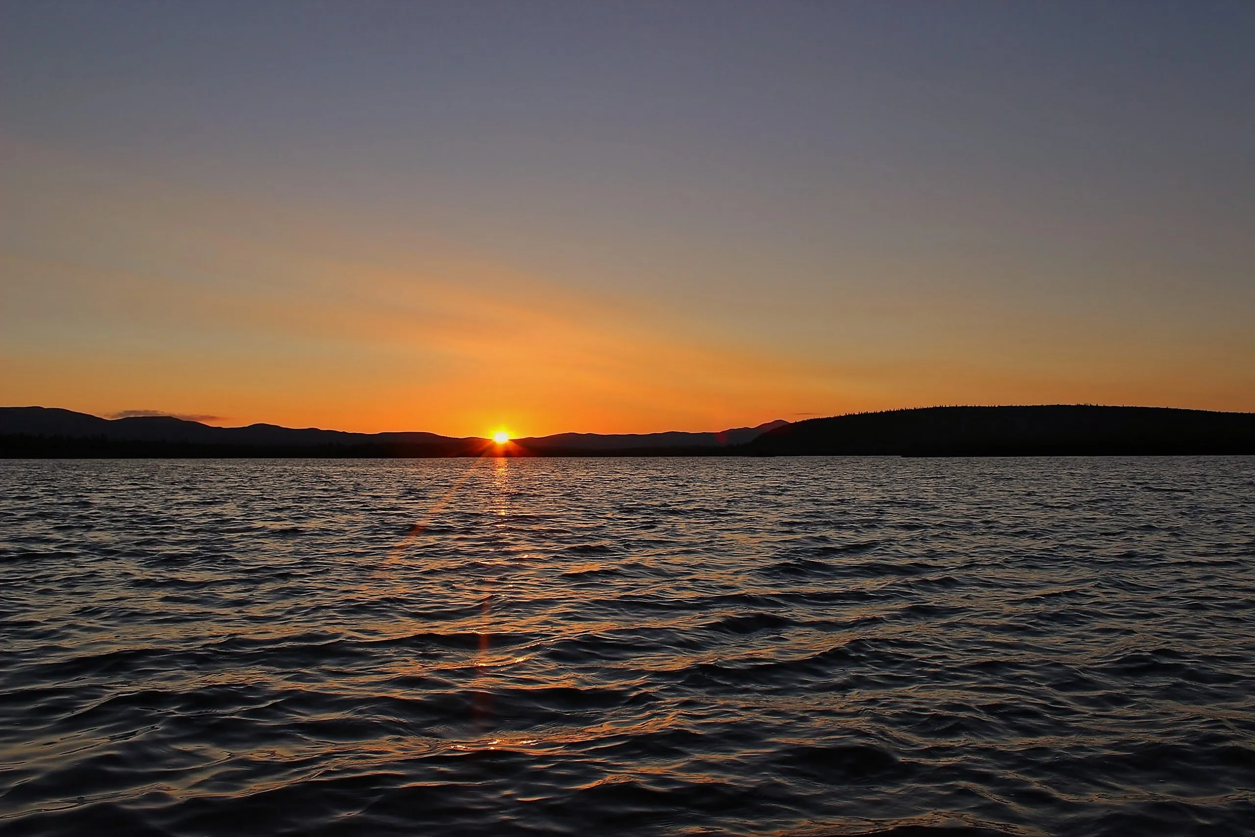Sun setting over the Yukon River with mountain silhouettes in Alaska.