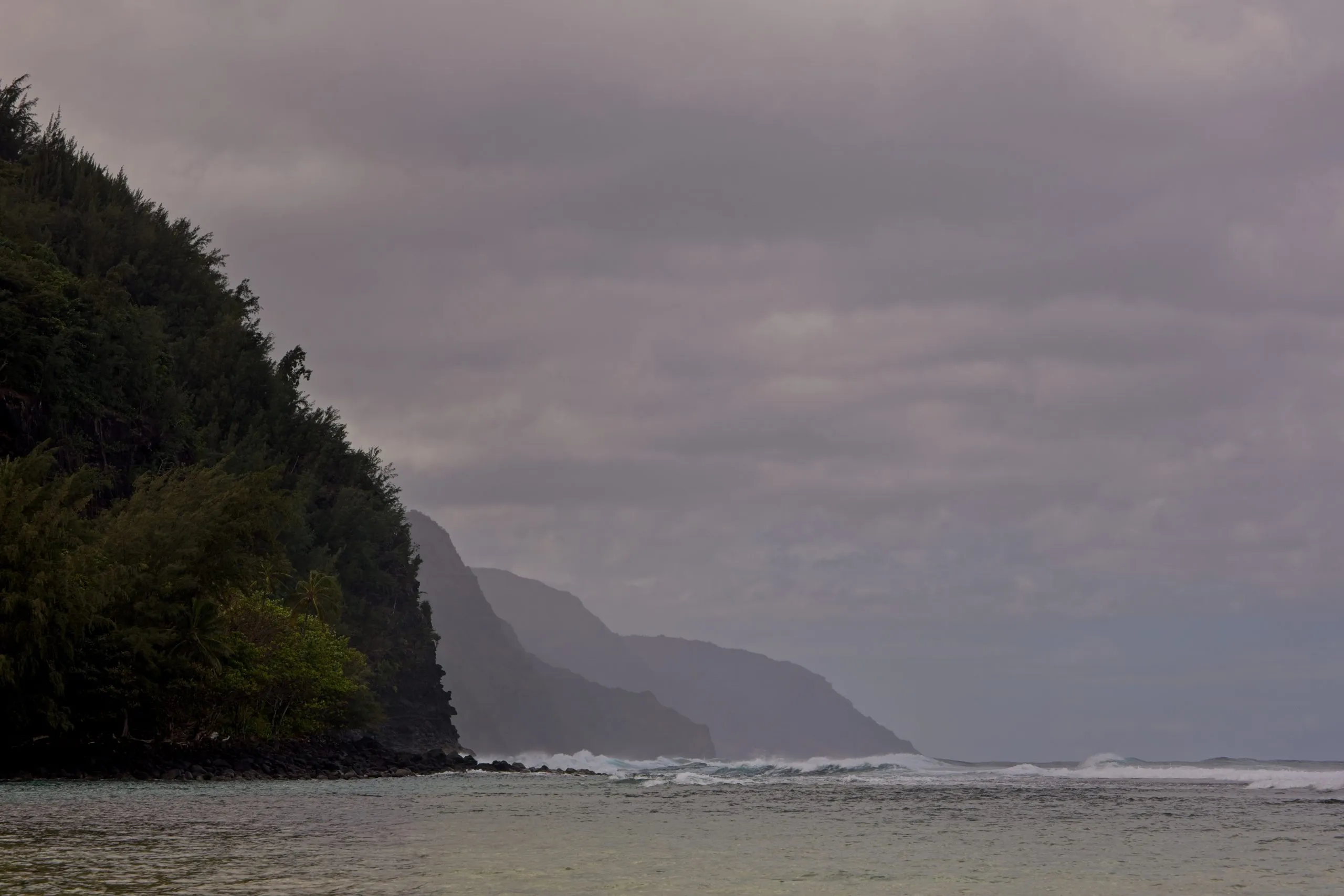 Nā Pali cliffs rising from the ocean under dark storm clouds on Kauai, Hawaii.