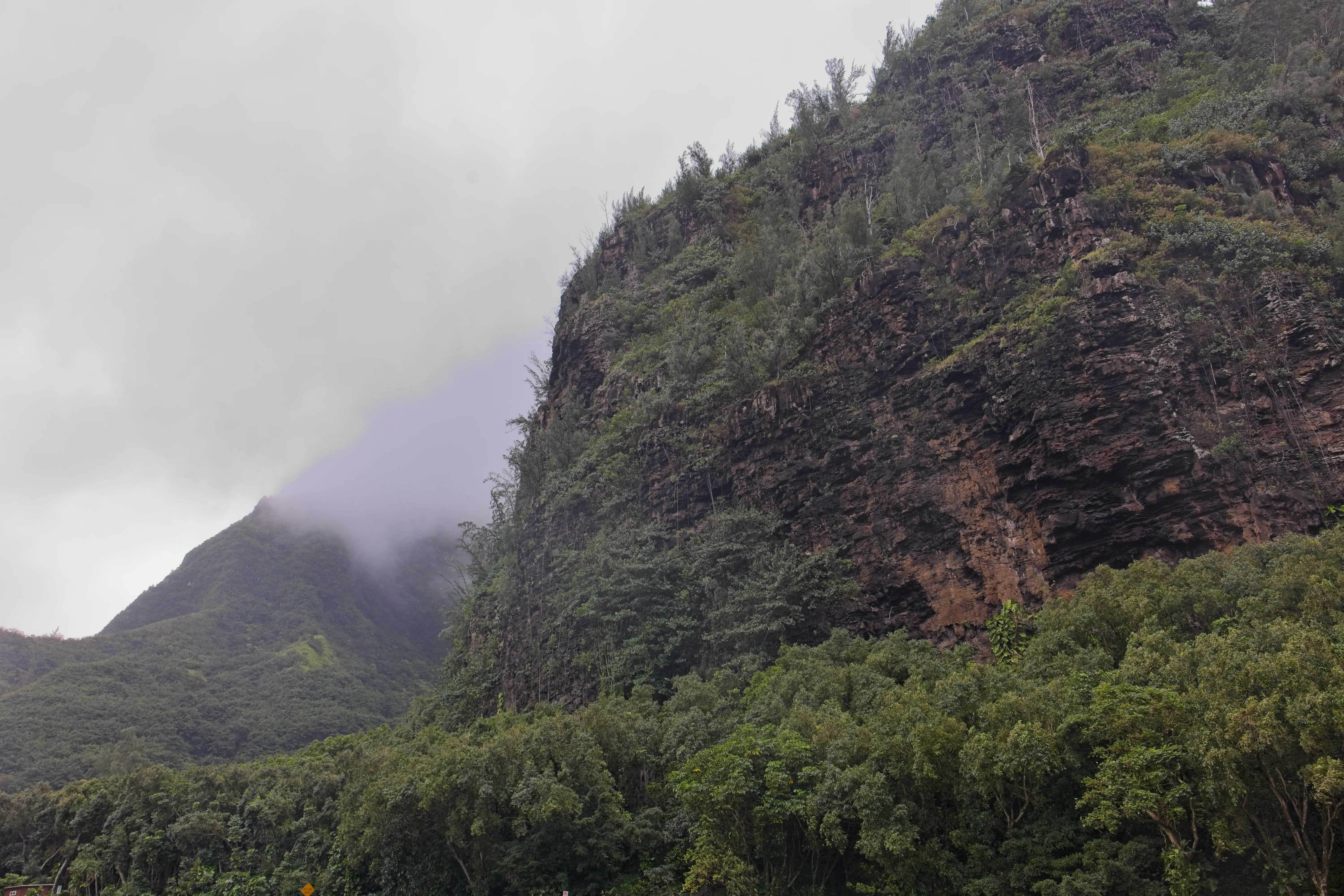 Steep Nā Pali cliff face with a mountain peak shrouded in clouds on Kauai, Hawaii.