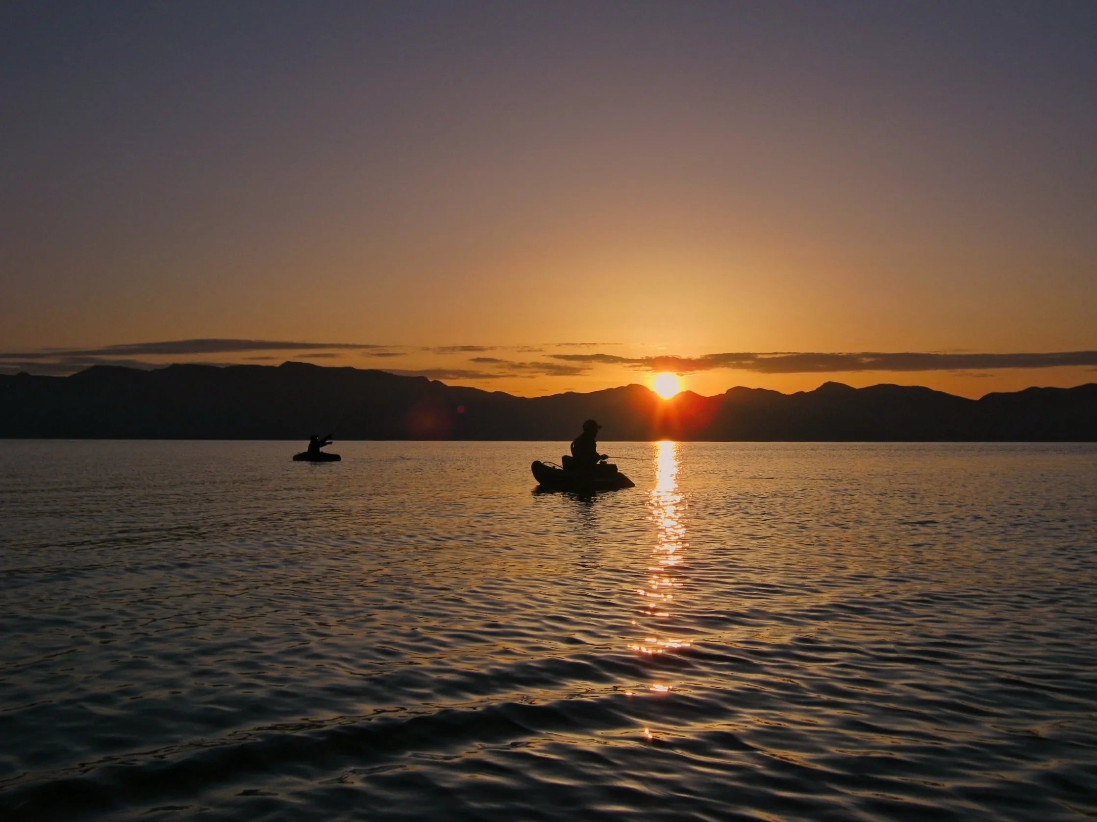 Two anglers in float tubes silhouetted against a golden sunset on Pyramid Lake, Nevada.