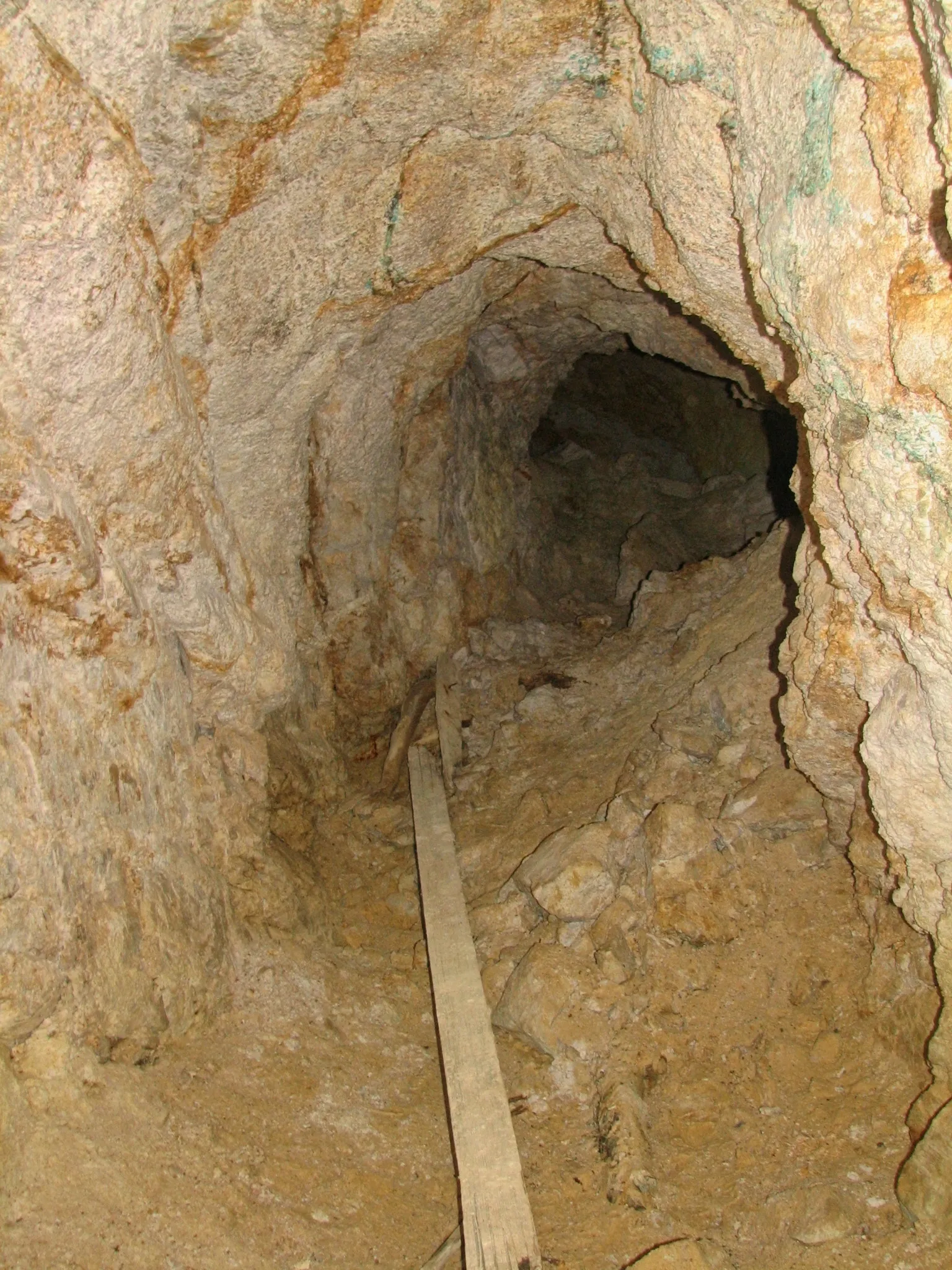 Narrow rocky mine passage with green and blue copper mineral staining on the walls.