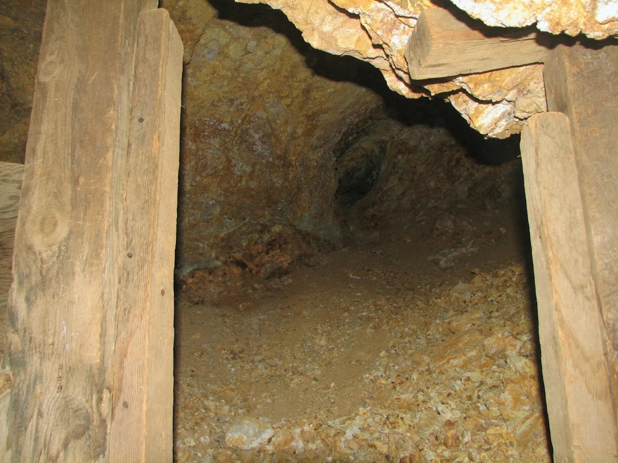 Timber-framed mine tunnel entrance with rocky walls receding into darkness.