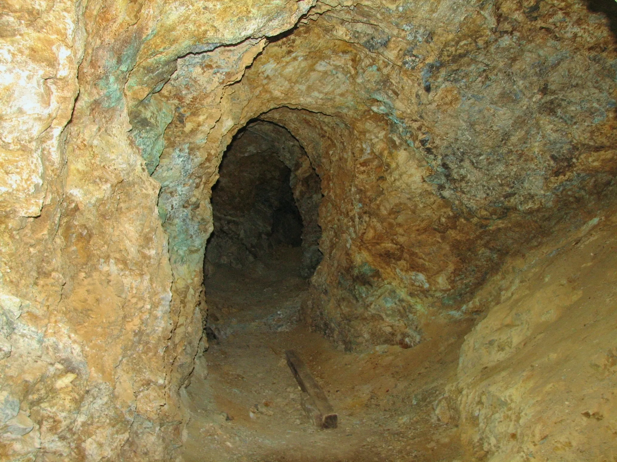 Rocky mine adit with turquoise copper staining and a wooden plank on the floor.