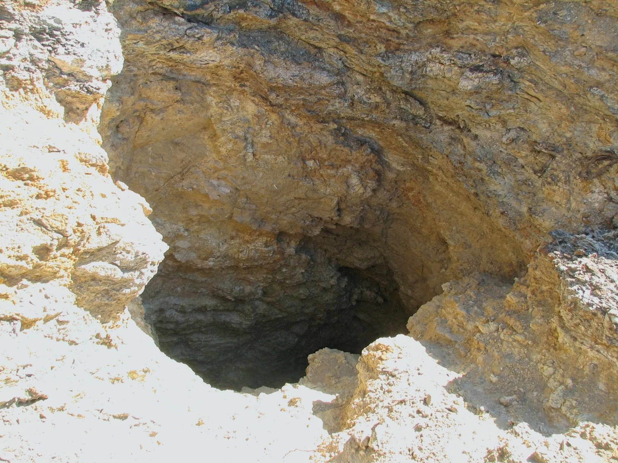 Jagged rocky opening of a vertical mine shaft dropping into darkness.
