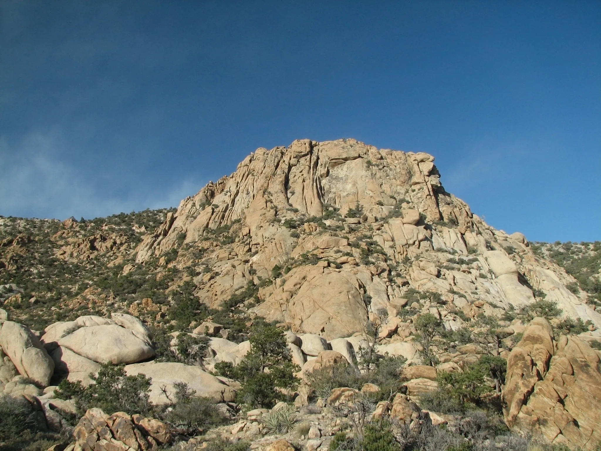 Craggy granite peak rising above boulders and desert scrub in the New York Mountains.