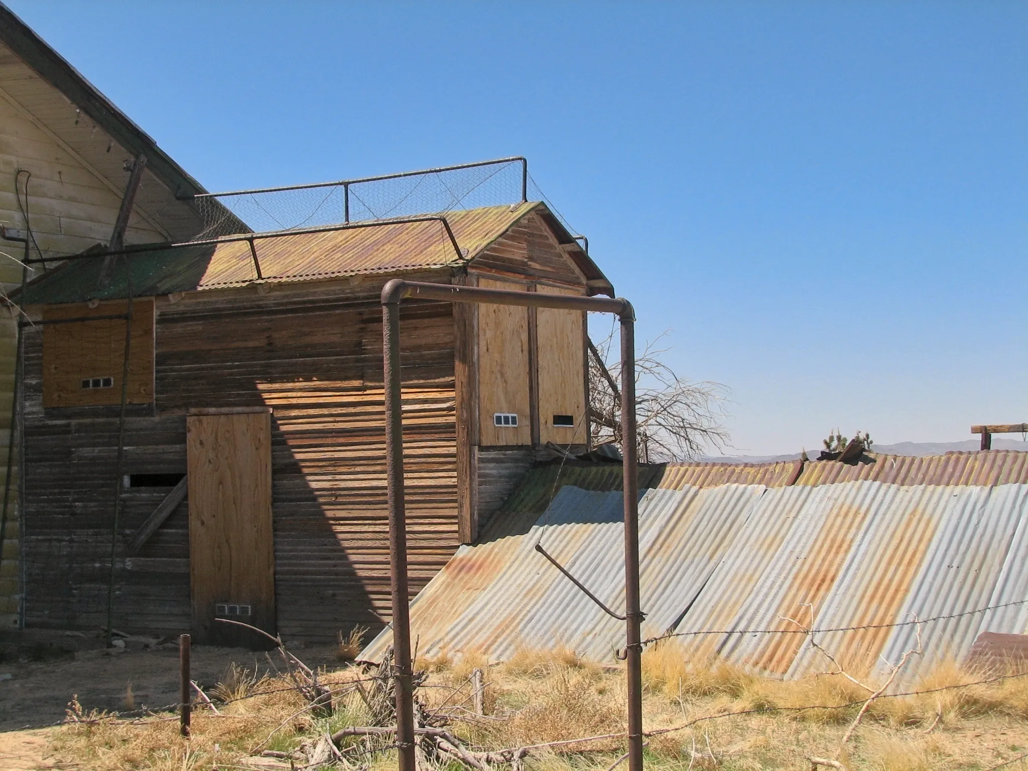 Weathered wooden and corrugated metal mine structures behind a barbed-wire fence.