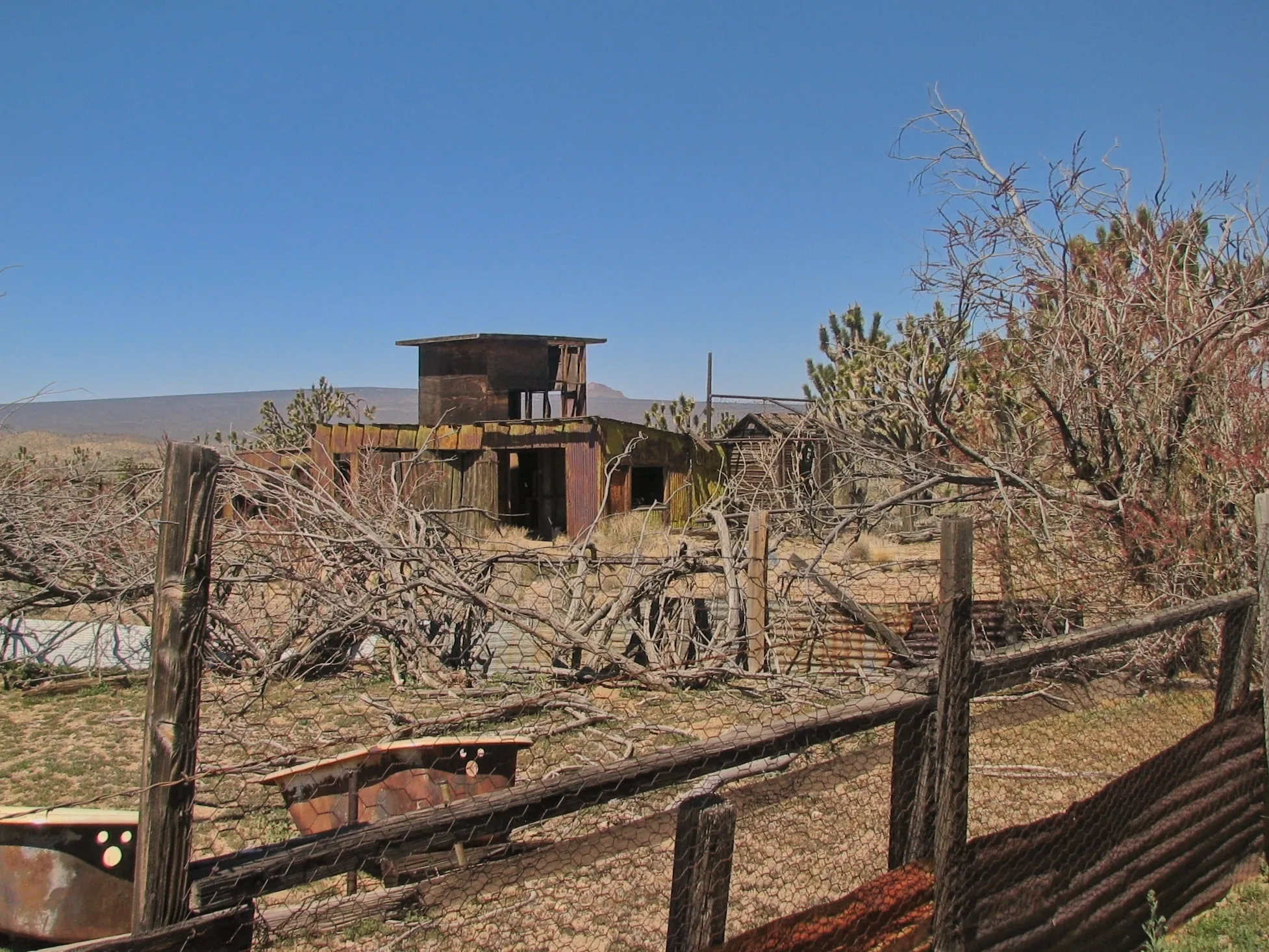 Dilapidated tiered wooden and metal mine building behind a wire fence.