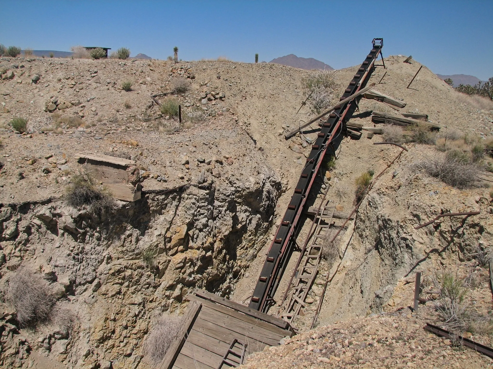 Rusted inclined conveyor belt descending into a rocky mine pit.