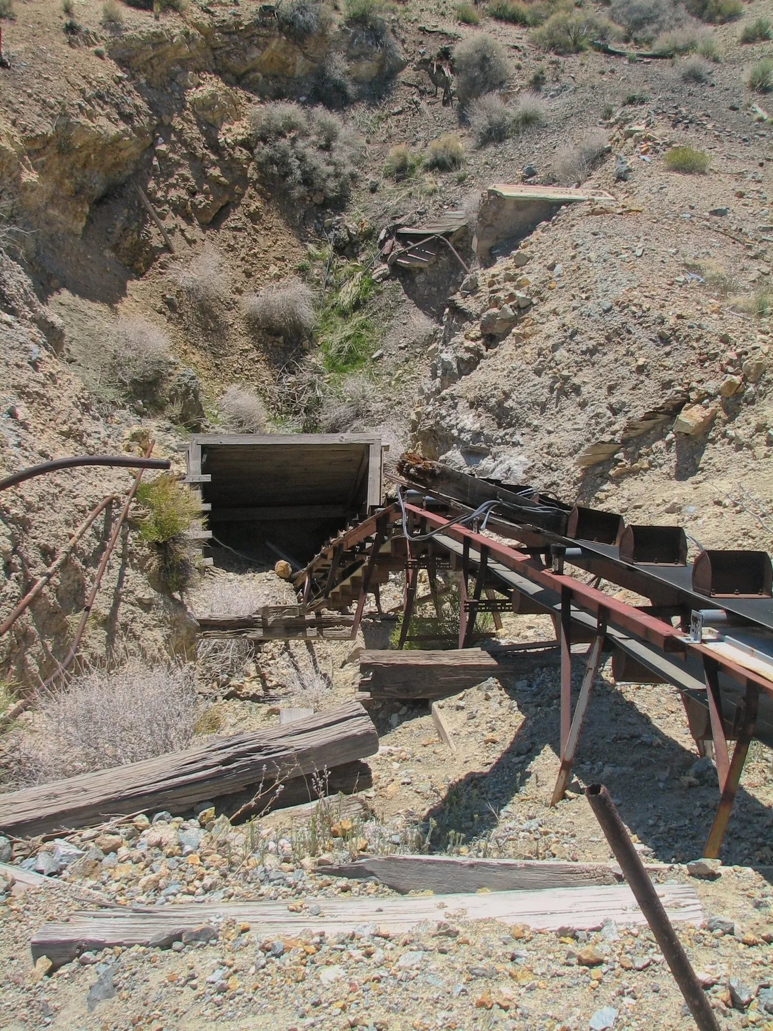Mine portal with rusted bucket conveyor in a rocky desert ravine.