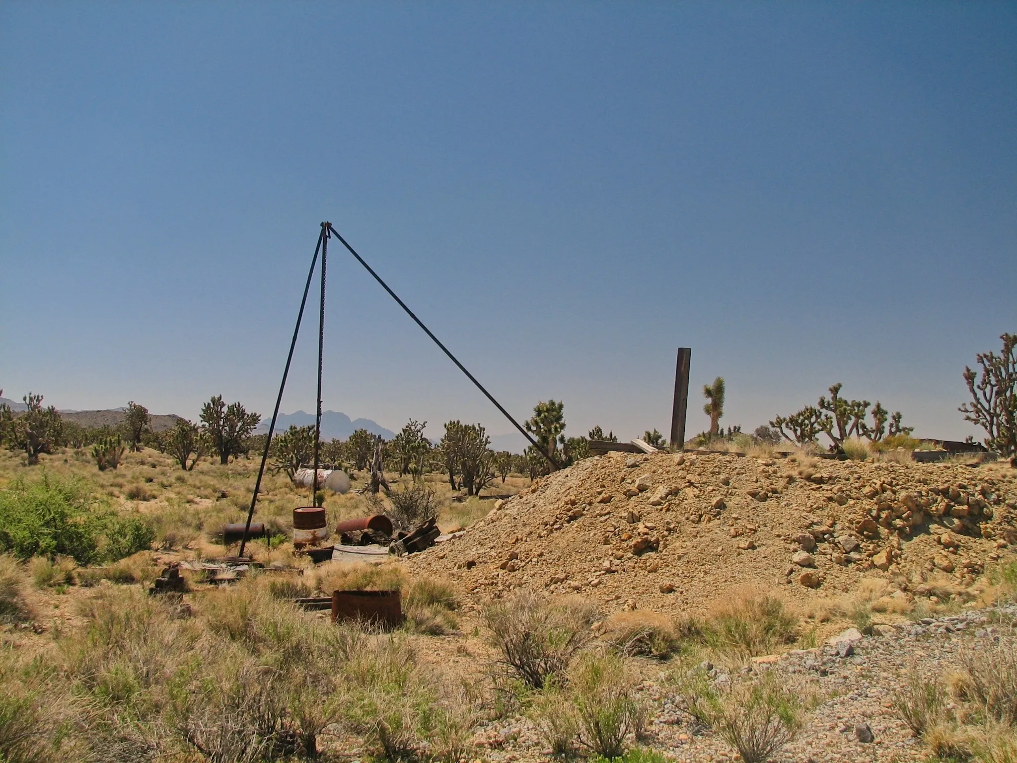 Rusted mining hoist tripod and tailings pile among Joshua trees at Death Valley Mine.