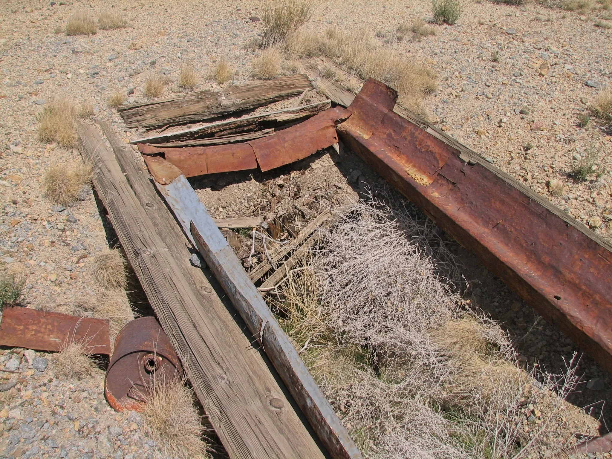 Wooden frame and rusted metal trough filled with desert brush debris.