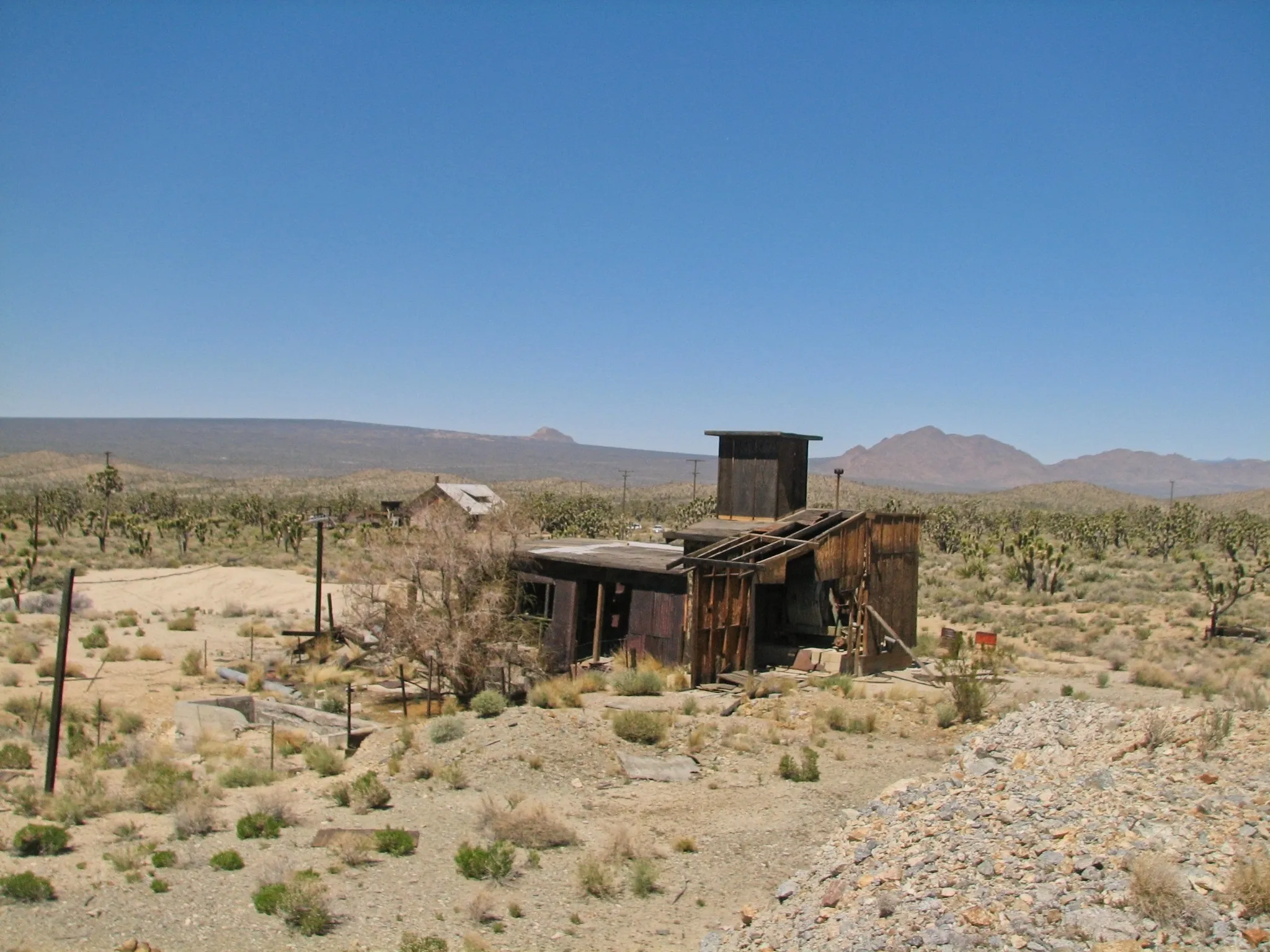 Wide view of dilapidated mine buildings and tailings pile with Joshua trees.