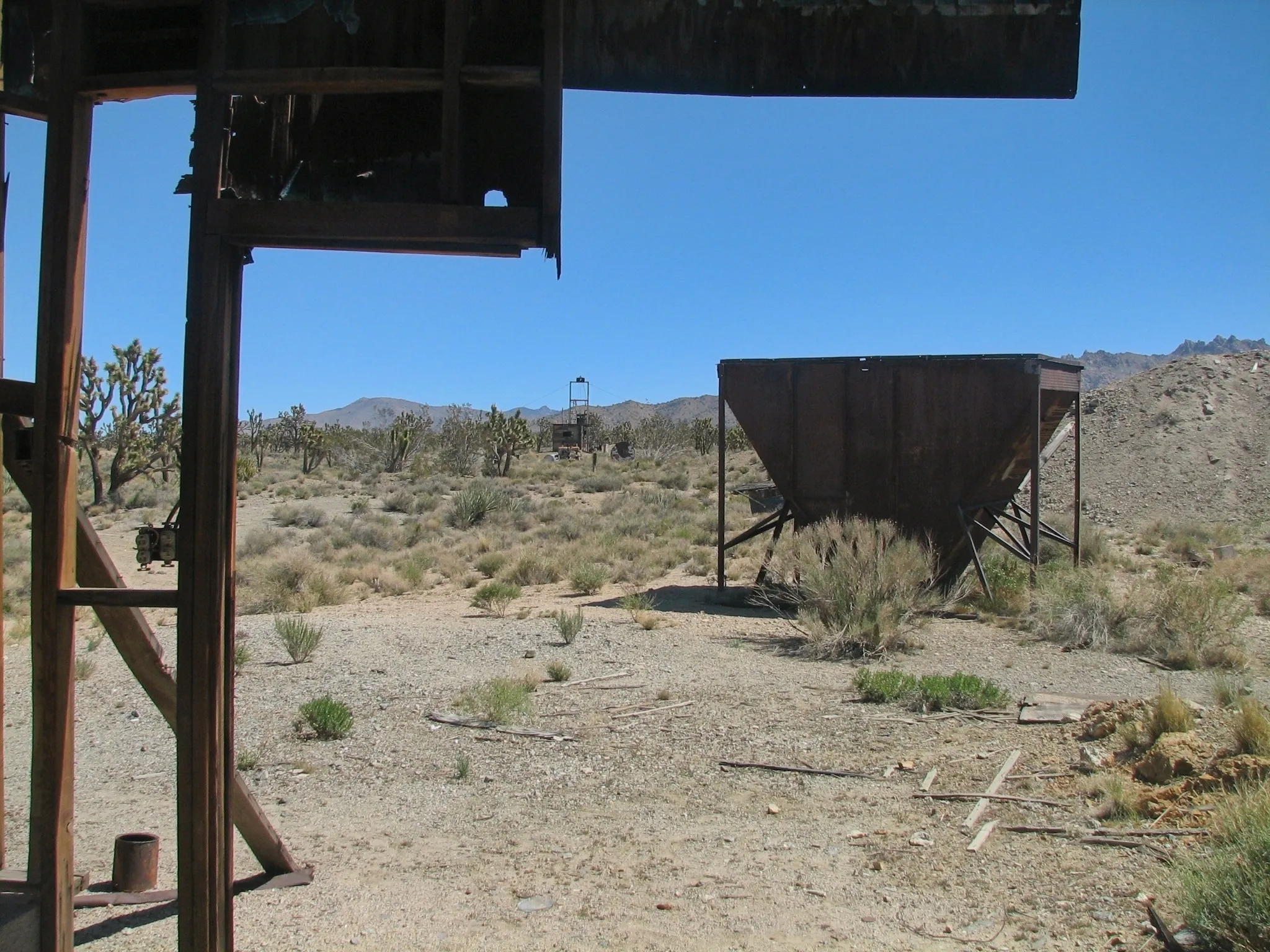 Rusty ore hopper and mine headframe viewed from inside a collapsed wooden building.
