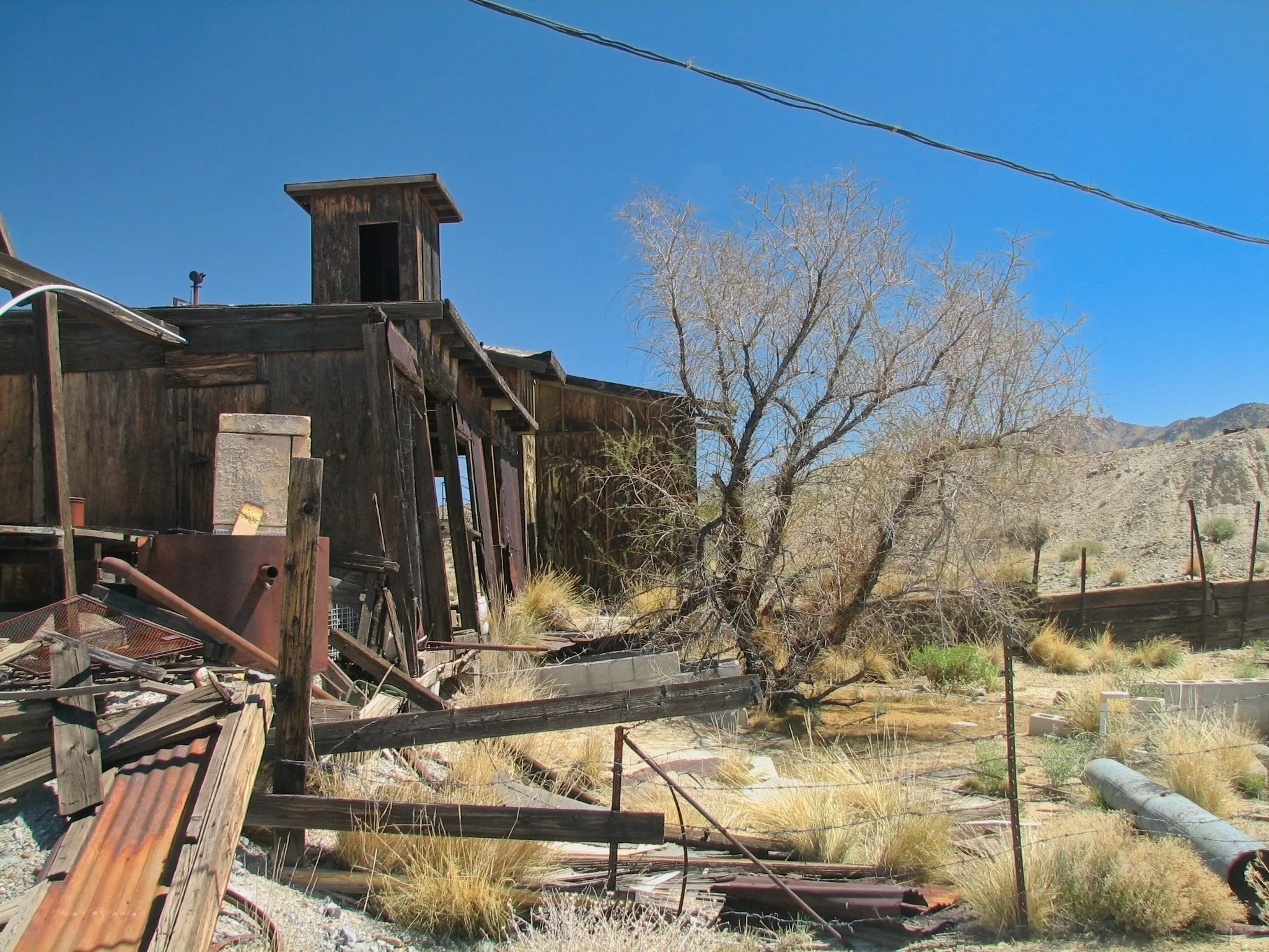 Collapsing wooden mine building surrounded by scrap metal and debris.