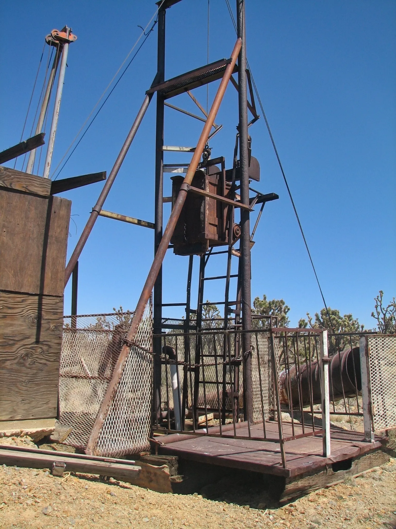 Rusted metal mine headframe with ore bucket against blue sky.