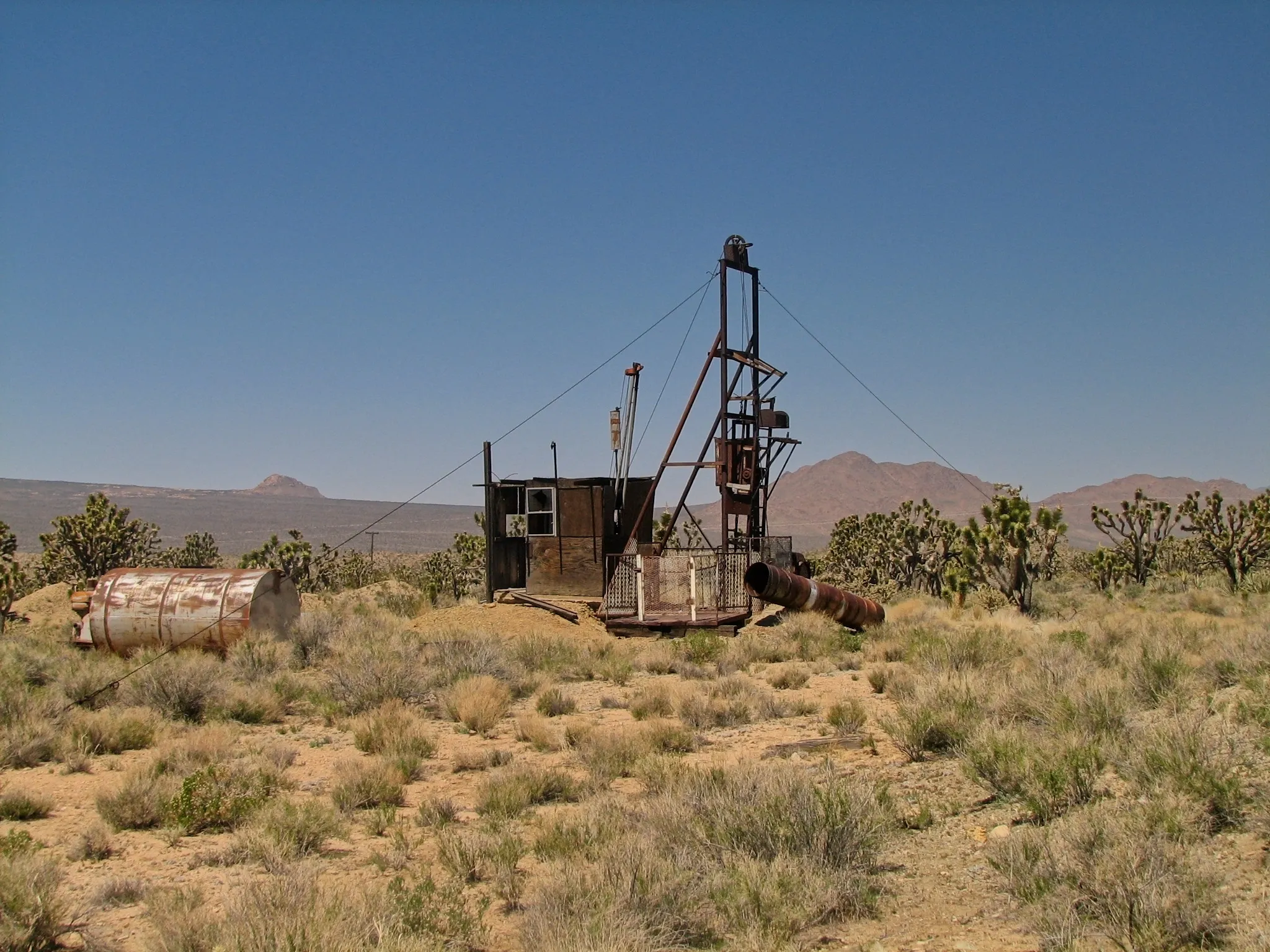 Rusted mine headframe and horizontal tank beside Joshua trees at Death Valley Mine.