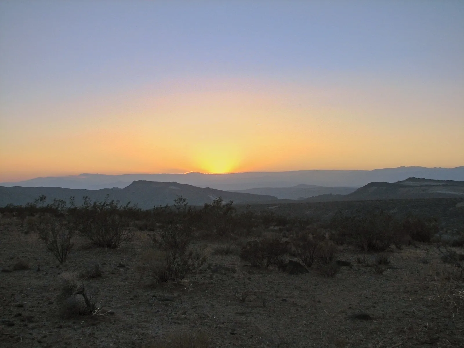Sun rising over layered desert hills in the Mojave Desert.