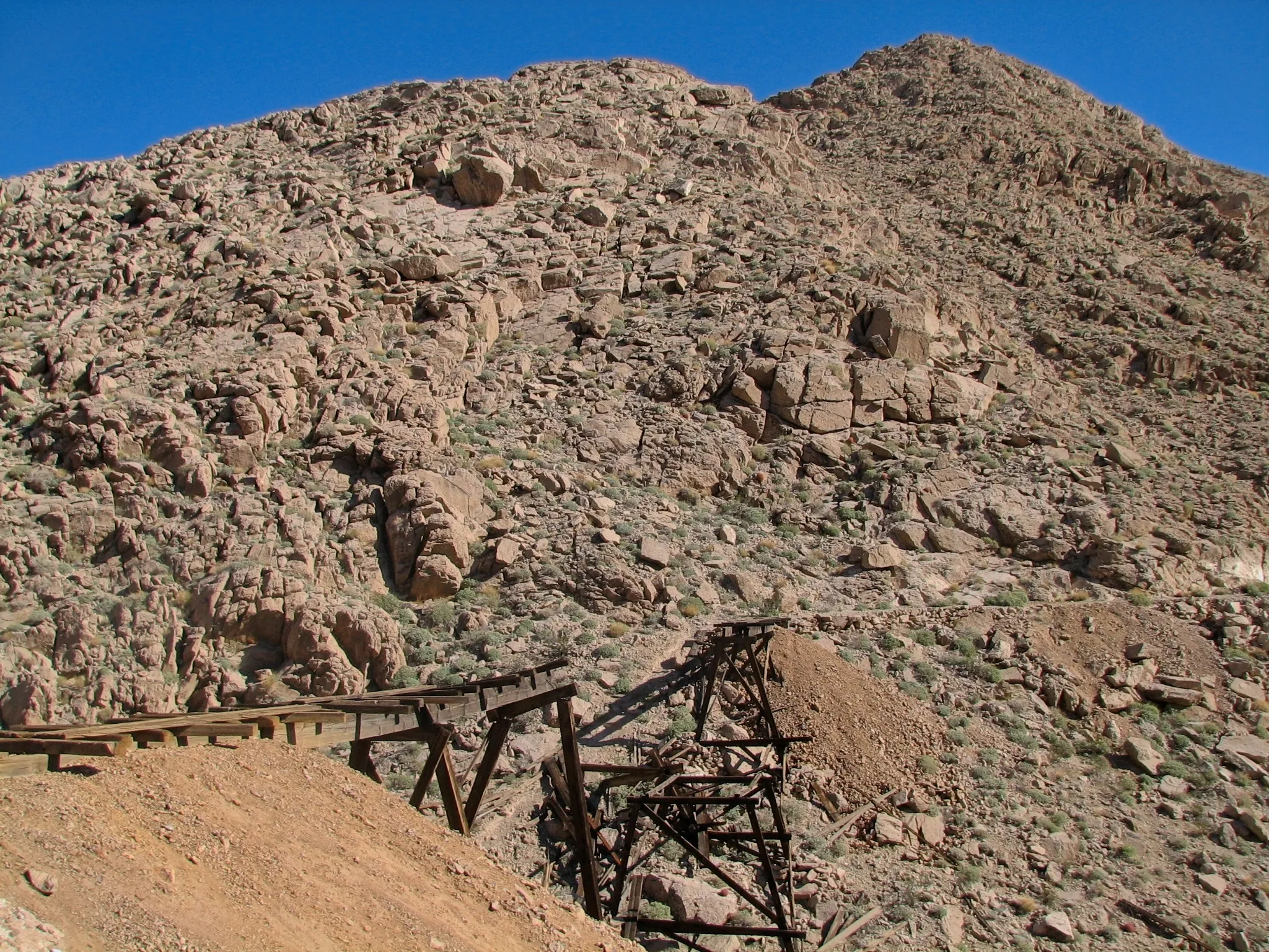 Collapsed wooden trestle and tailings pile on desert mountainside at War Eagle Mine.