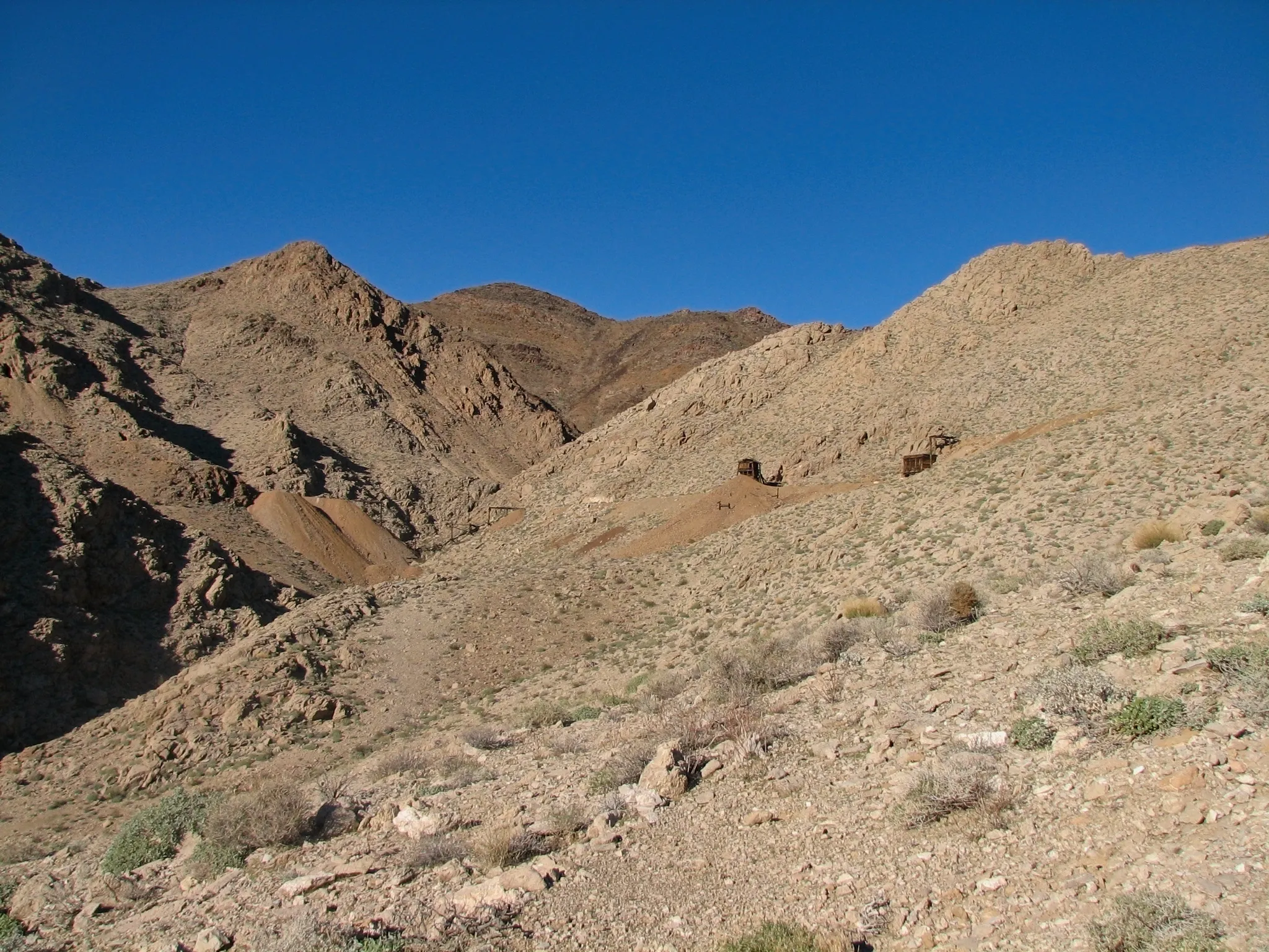 Desert hills with small wooden mine frames on tailings piles.
