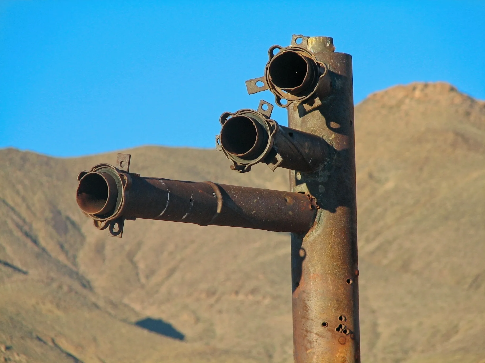 Close-up of rusted pipe branches against desert mountains.