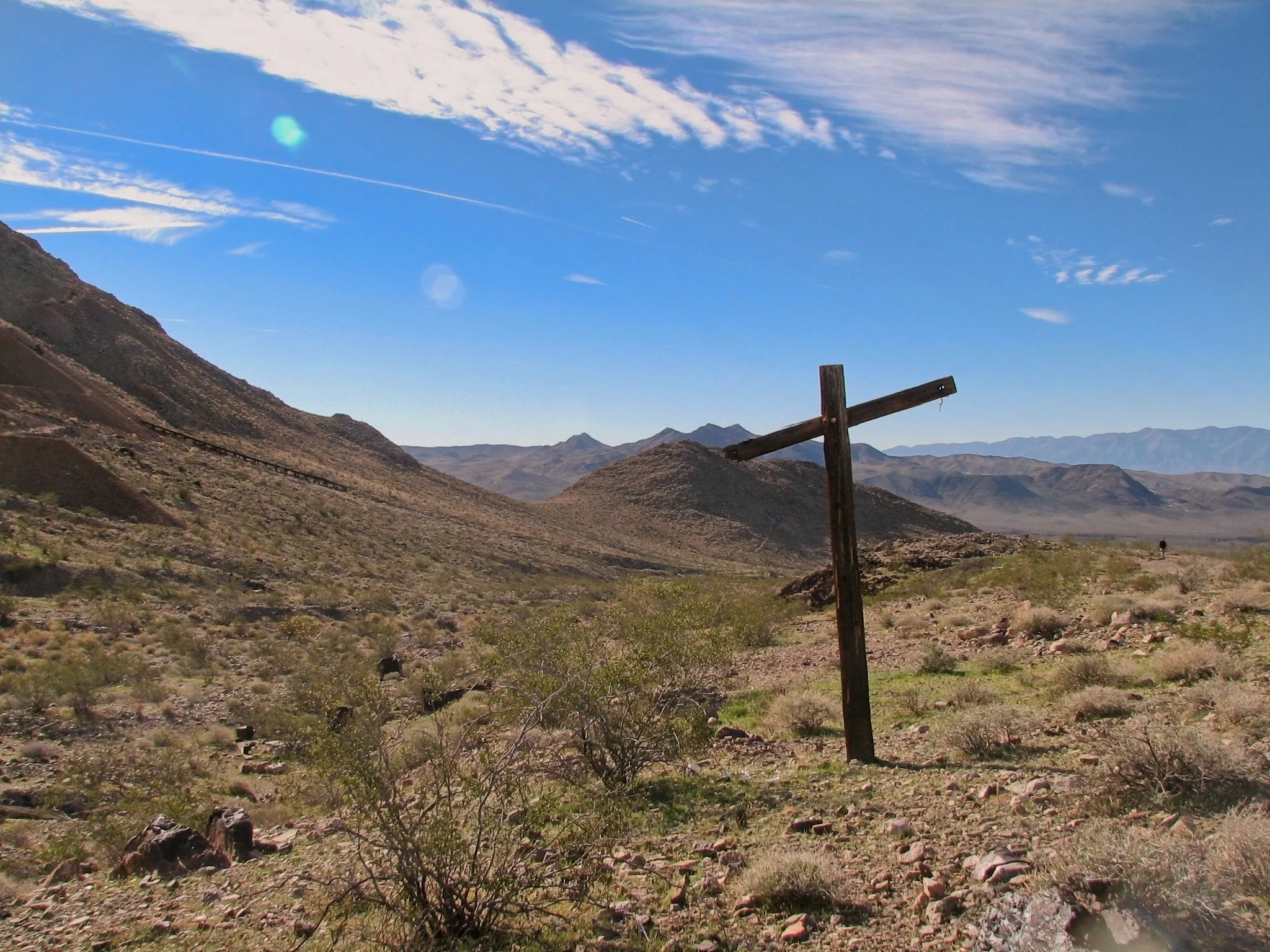 Wooden cross standing on rocky hillside above desert valley.