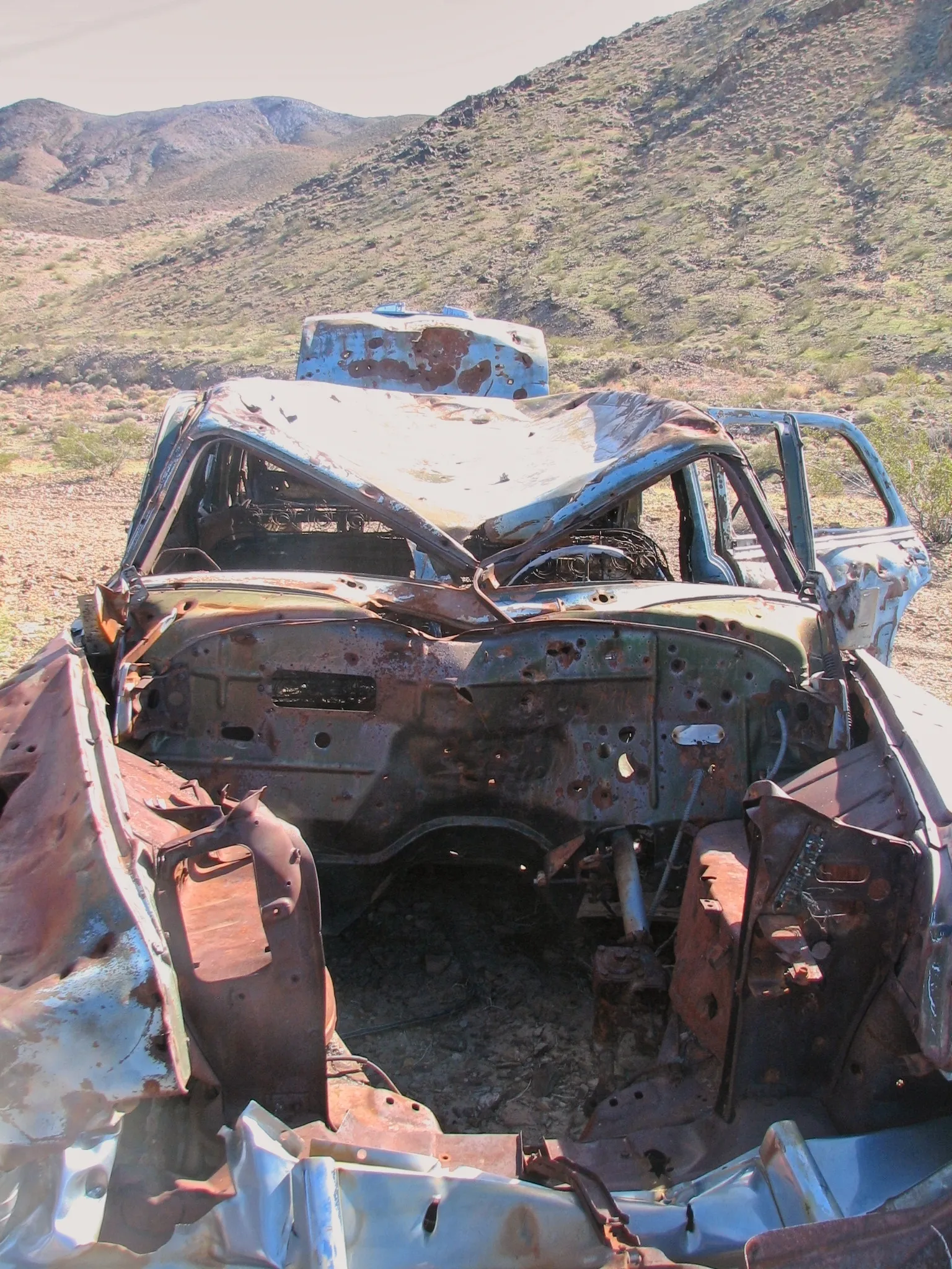 Bullet-riddled rusted car with crushed roof in desert near War Eagle Mine.