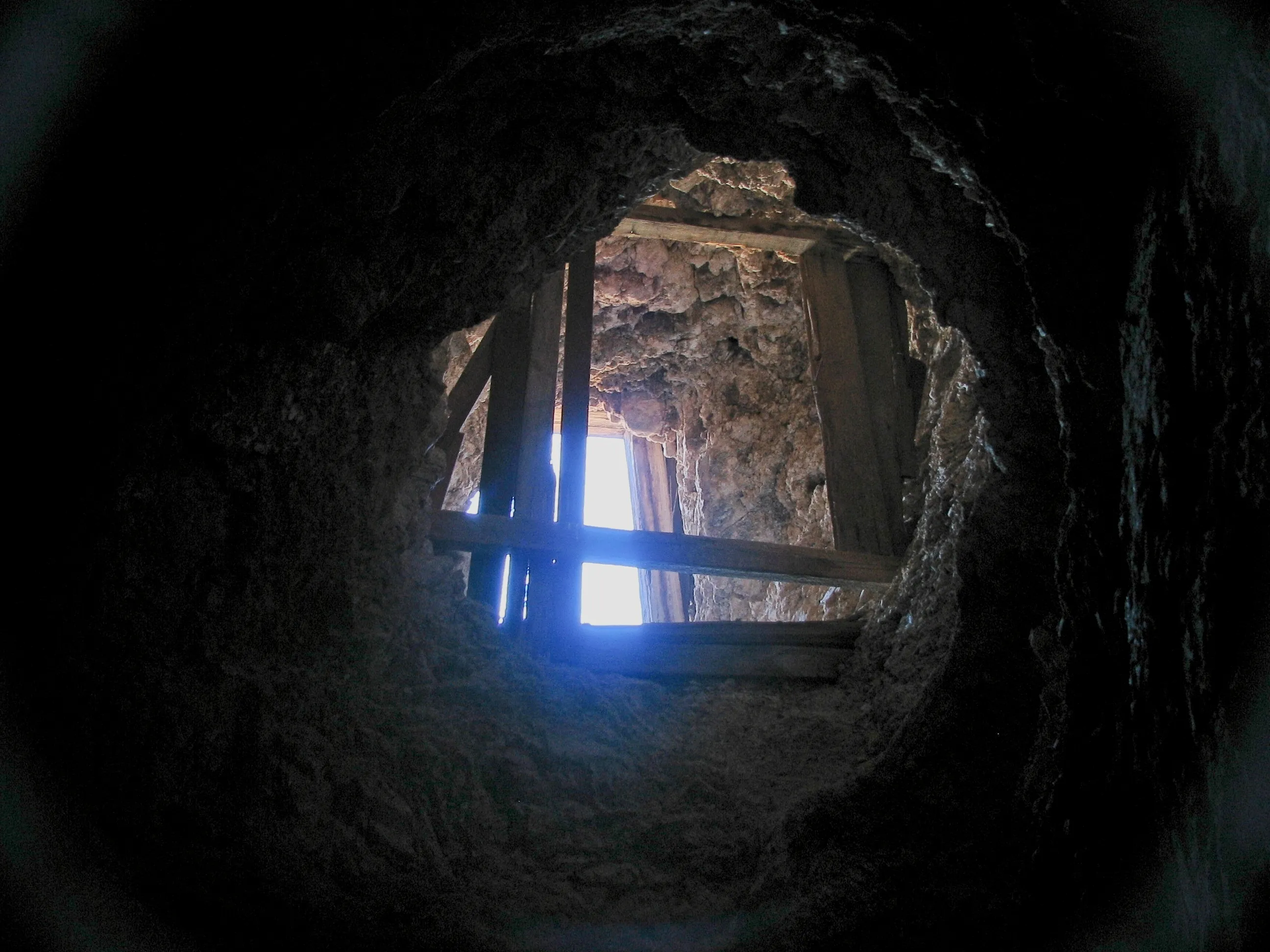 Daylight through wooden shoring seen from inside dark mine shaft.