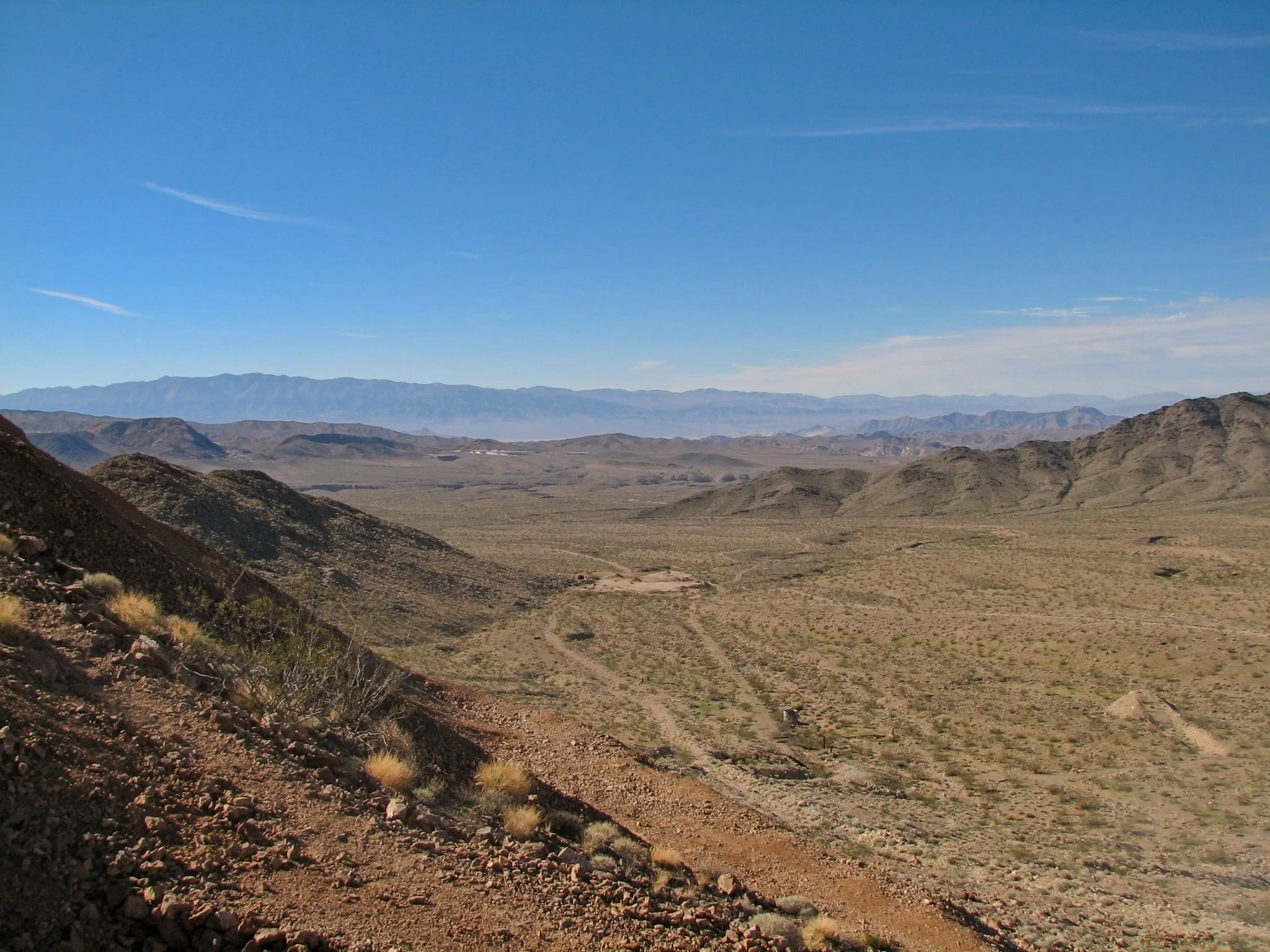 Wide desert valley with winding tracks seen from rocky hillside.
