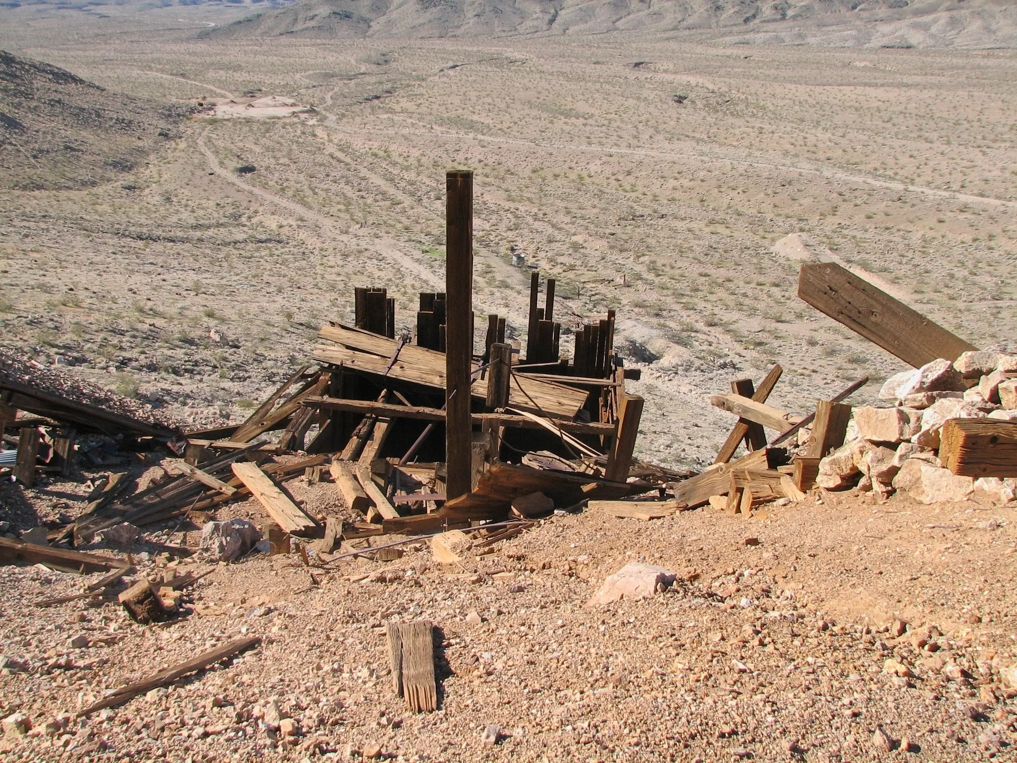 Collapsed wooden mine structure on hillside above desert valley.
