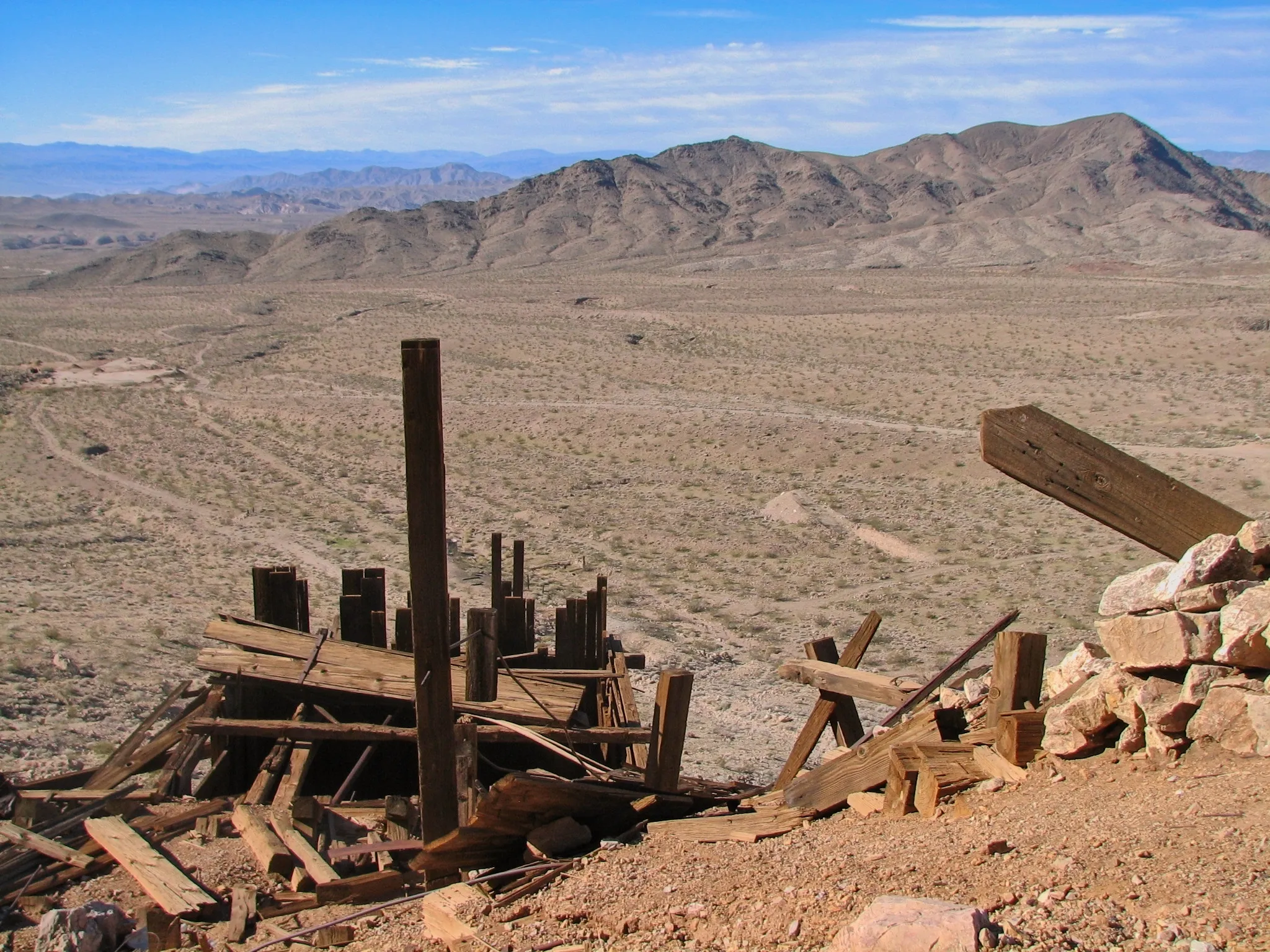 Wooden mine ruins overlooking vast desert valley from hillside.