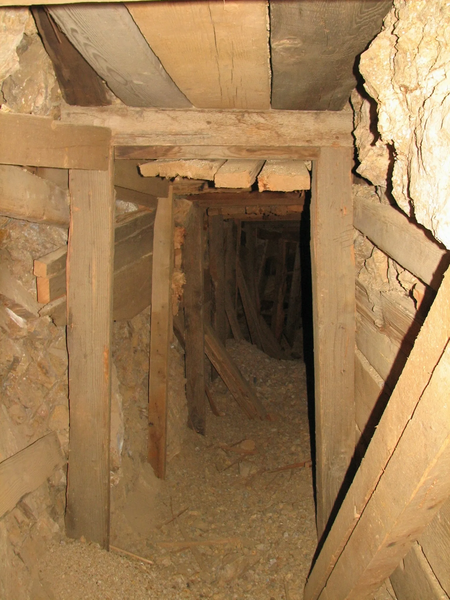 Timber-lined mine tunnel with gravel floor fading into shadow.