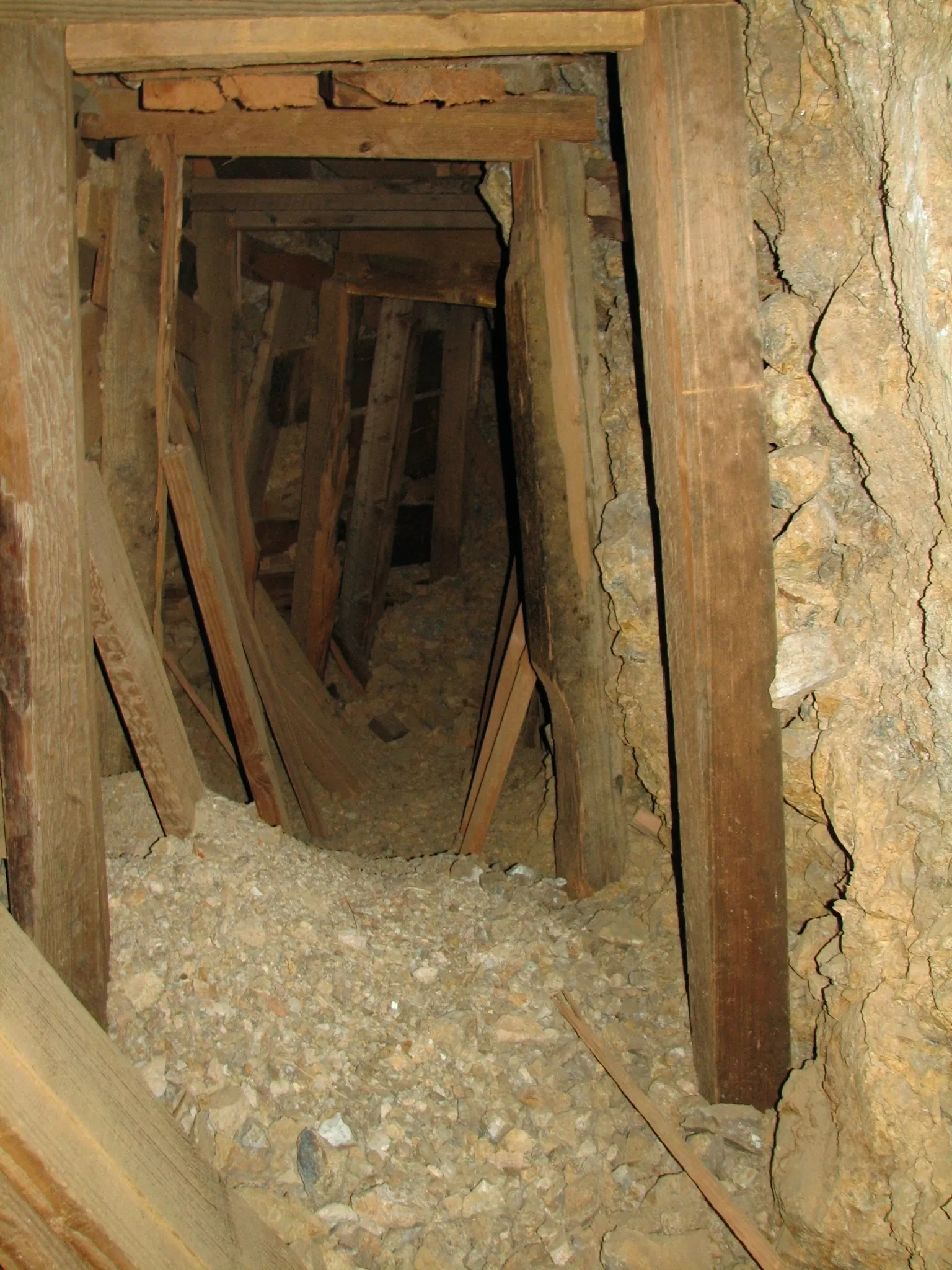 Timber-framed mine tunnel with gravel floor receding into darkness.