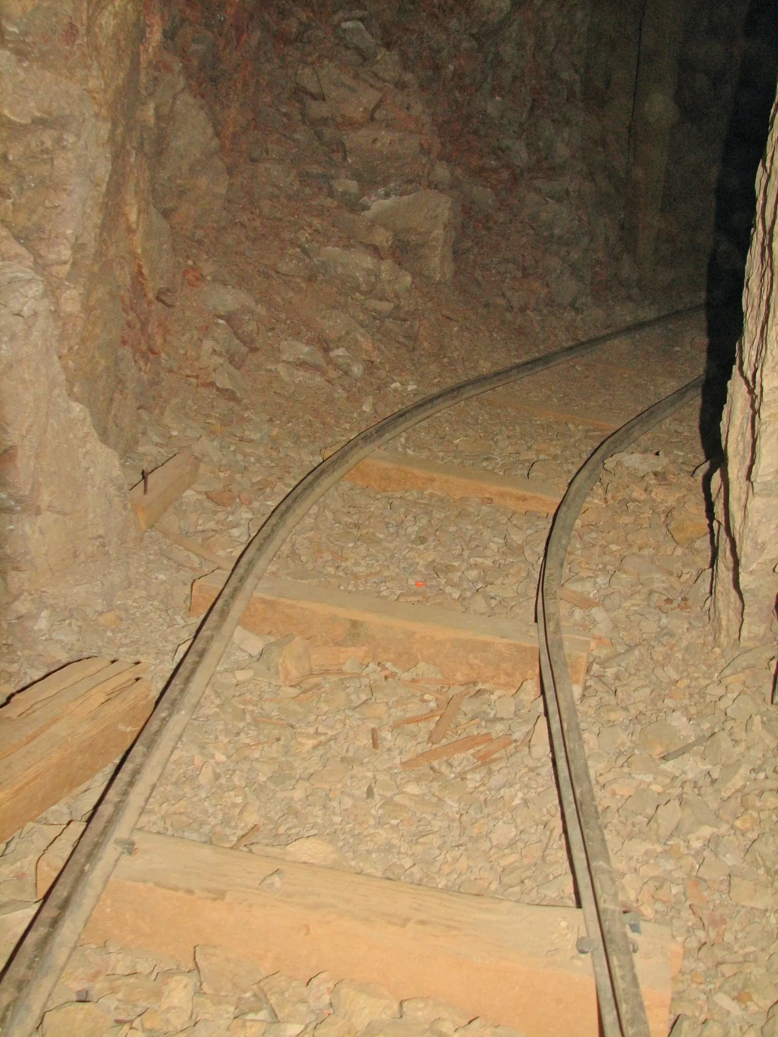 Curved narrow-gauge mine tracks inside rocky underground tunnel.