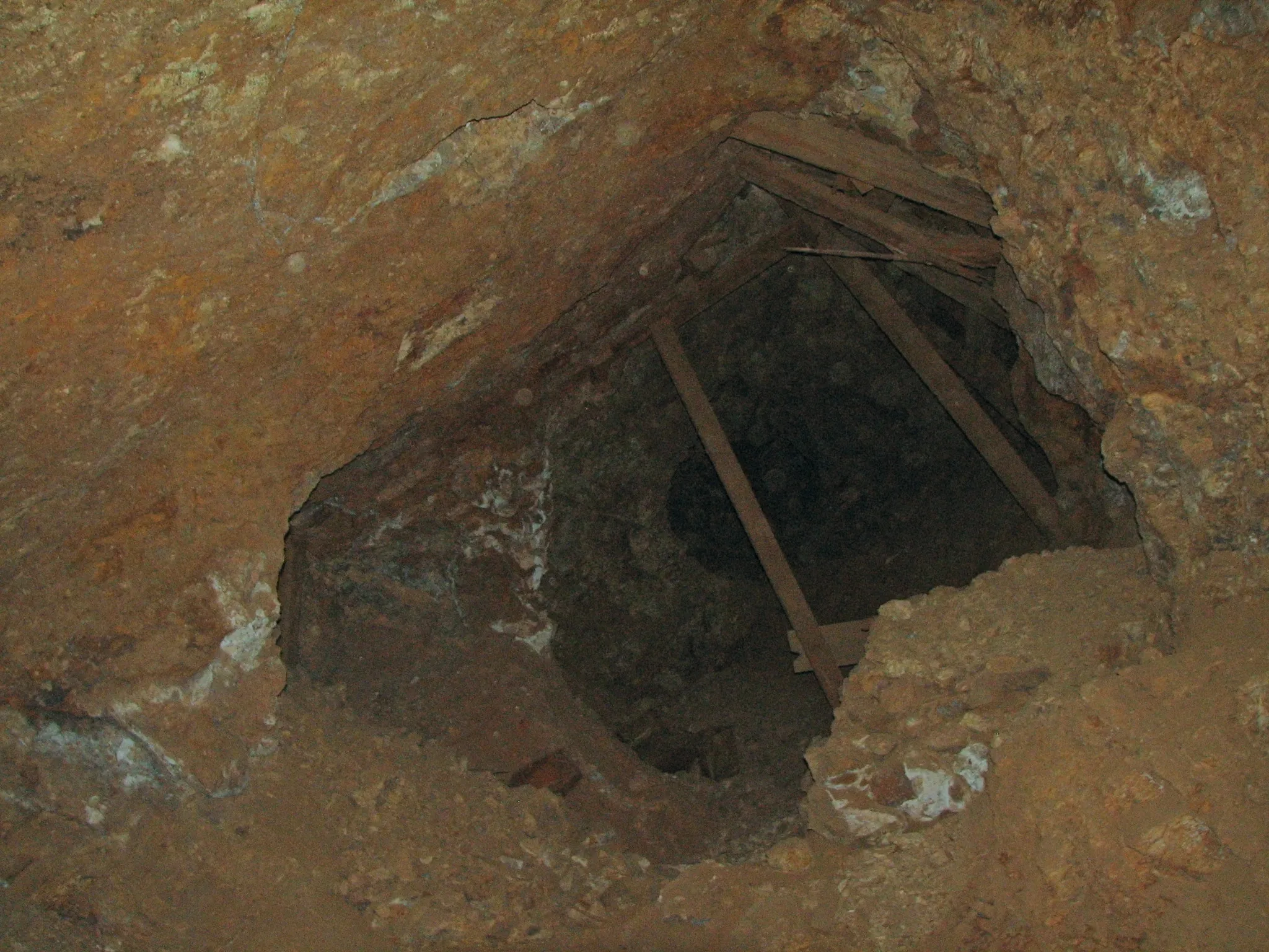 Timber-framed opening descending into dark mine shaft.