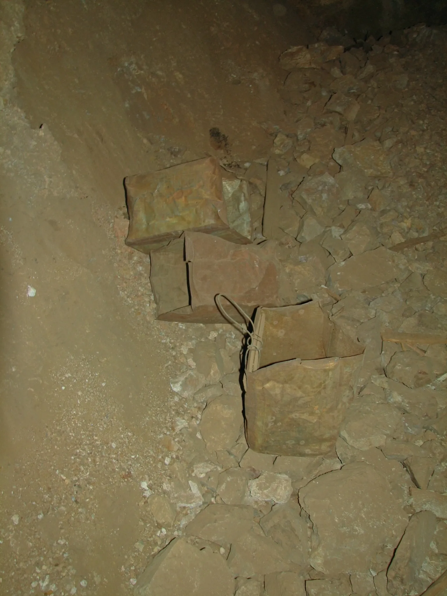 Rusted metal cans on rocky floor inside mine tunnel.