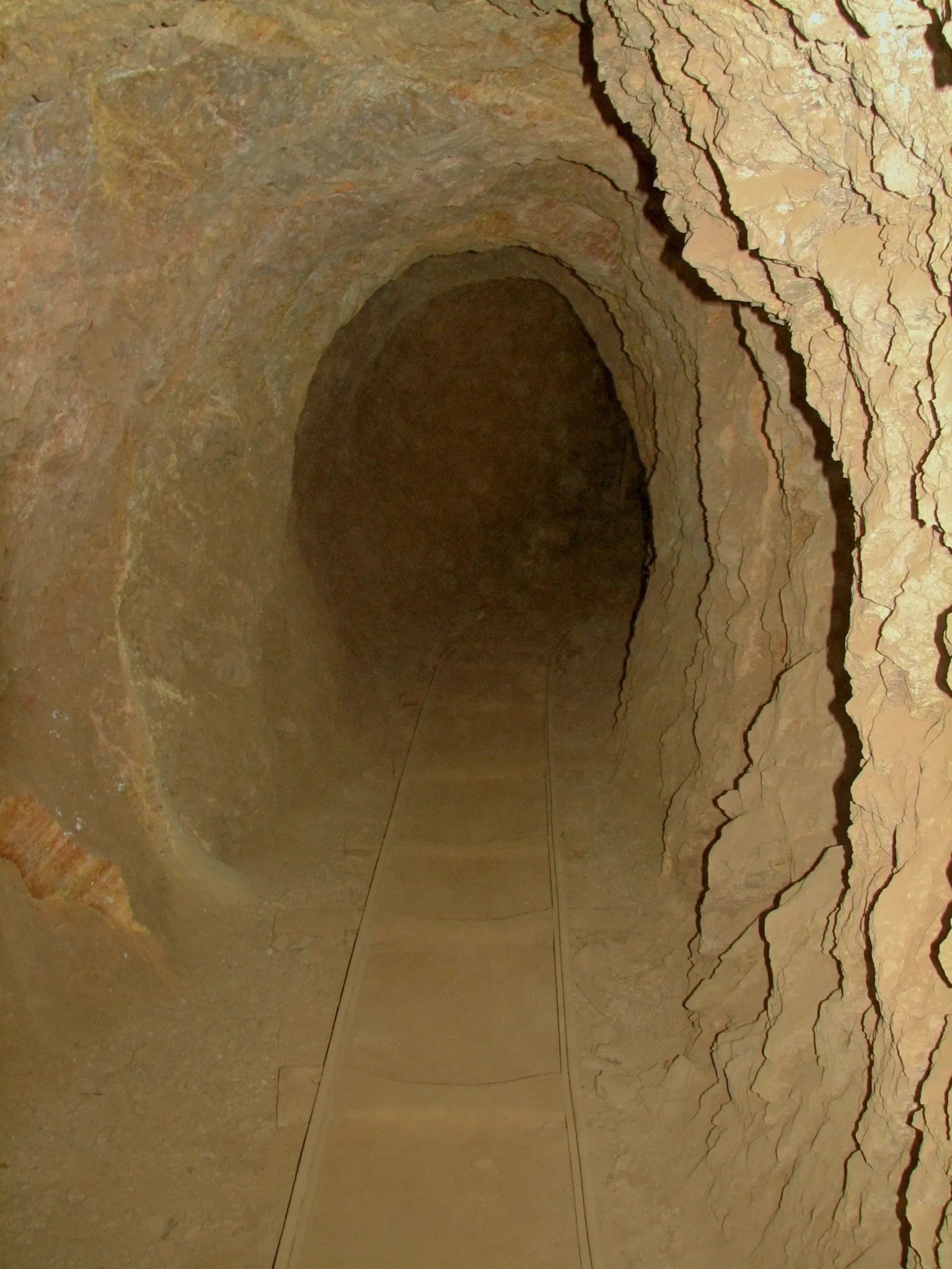 Narrow-gauge rails curving into darkness inside rocky mine tunnel.