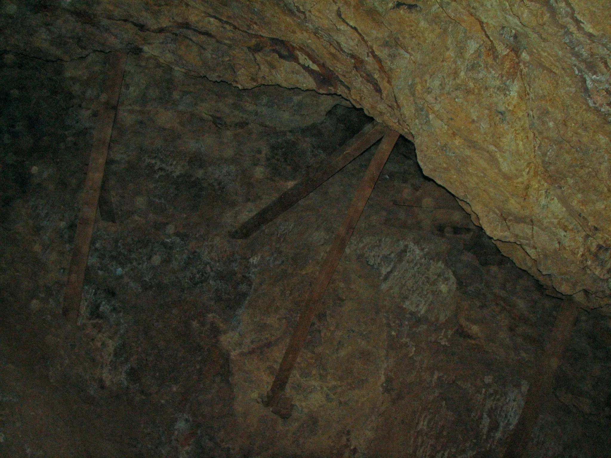 Weathered support beams bracing rocky mine cavern wall.