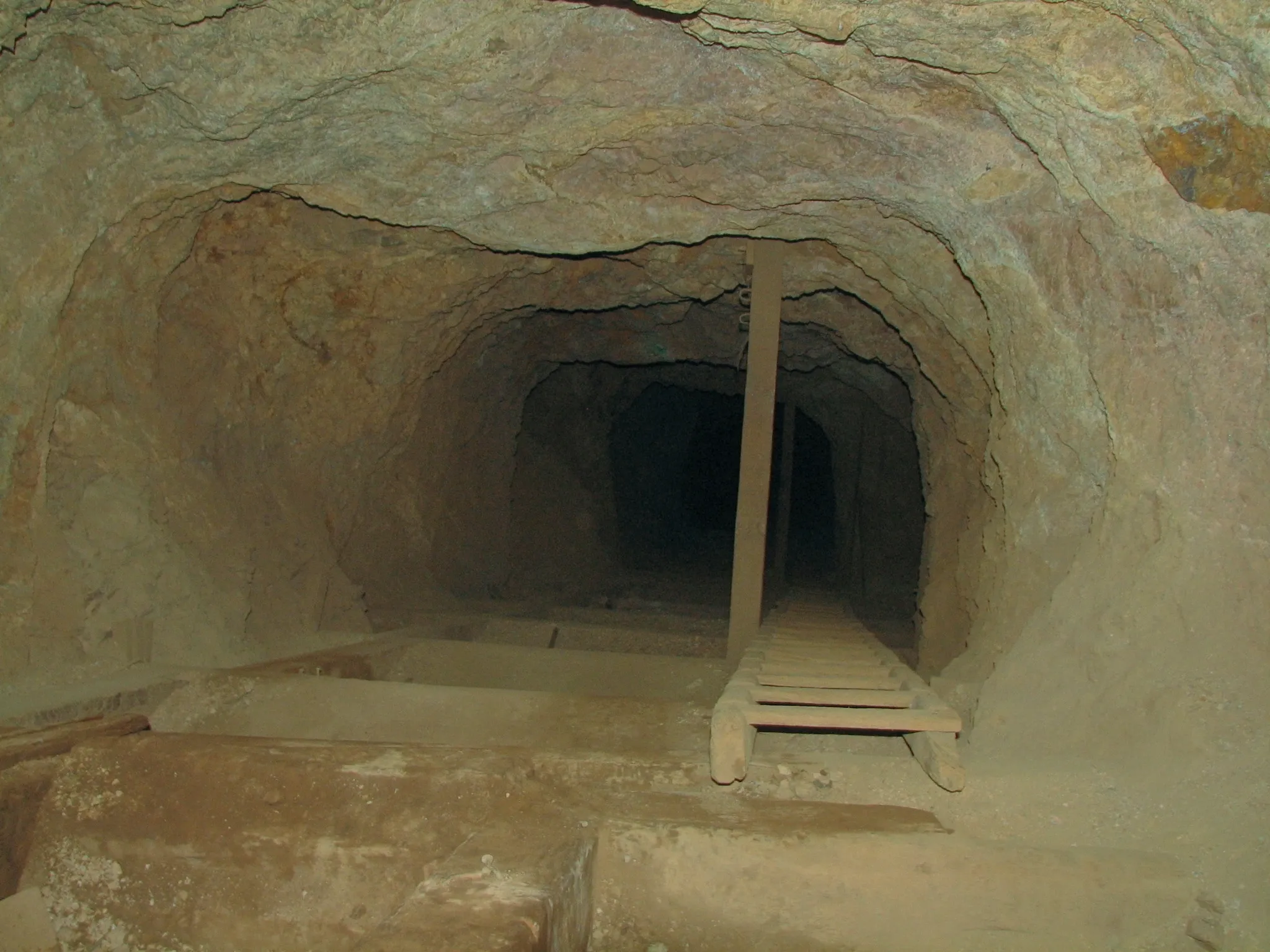 Wooden ladder across dusty ledge inside rocky mine tunnel.