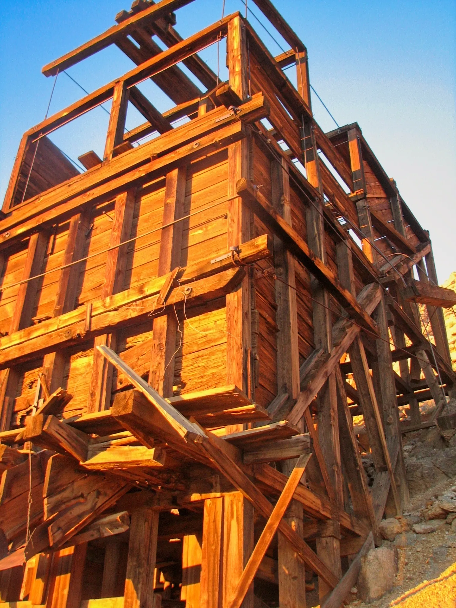 Wooden mine headframe glowing in golden sunset light on hillside.