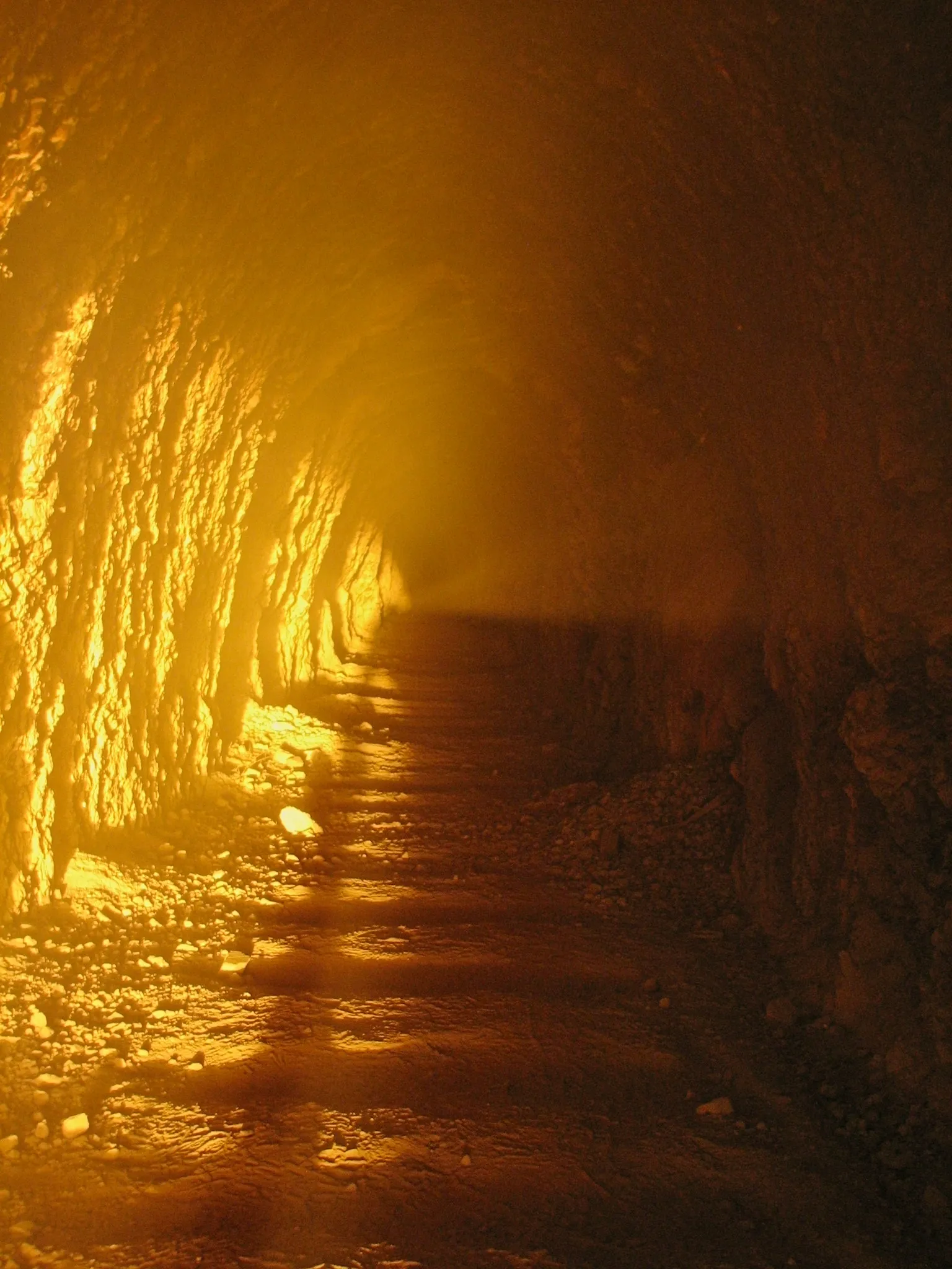 Sunlit mine tunnel with long shadows stretching into dusty darkness.