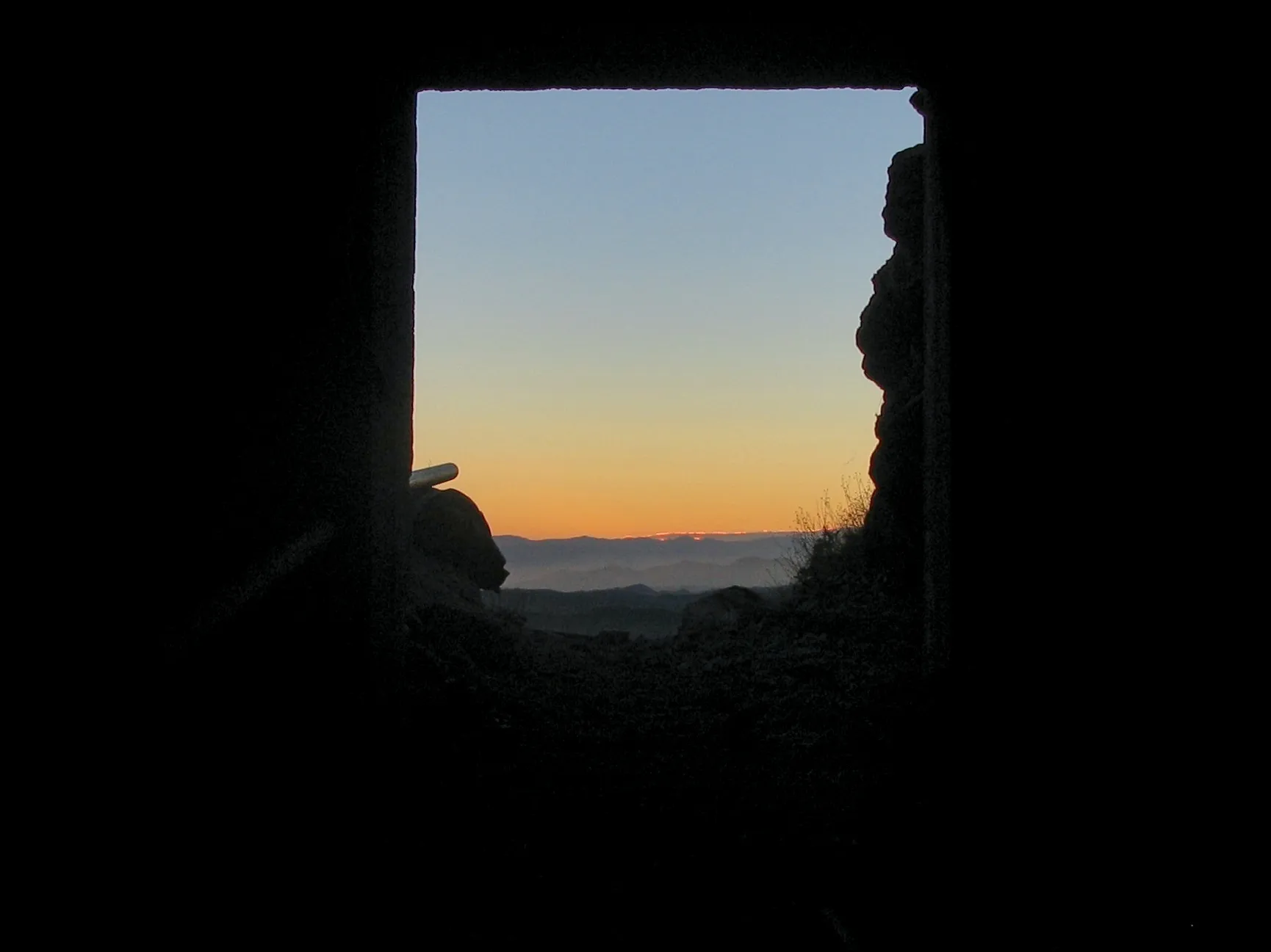 Sunset over distant mountains viewed through mine tunnel opening.