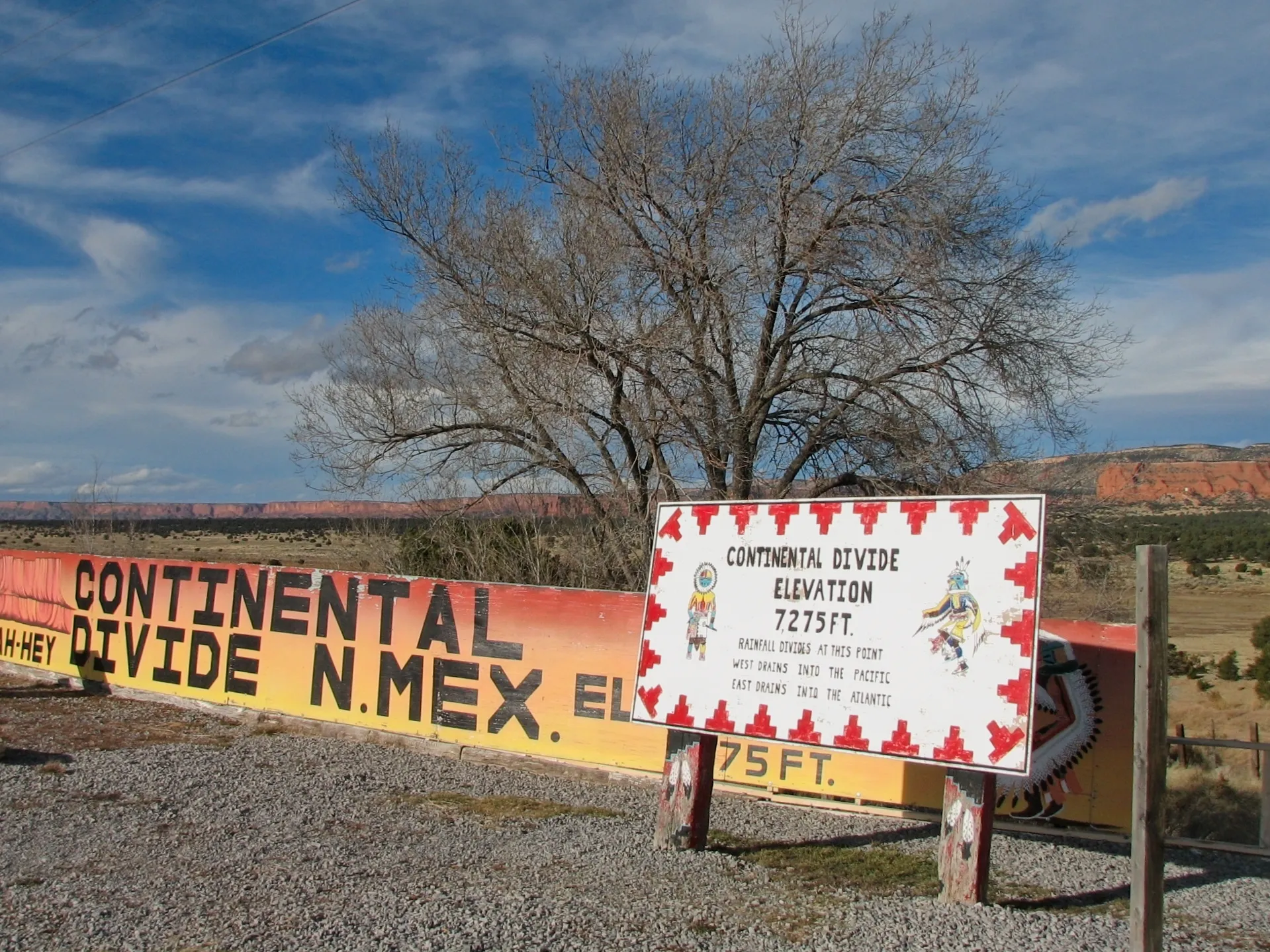 Continental Divide elevation marker signs with red mesas in the background in New Mexico.