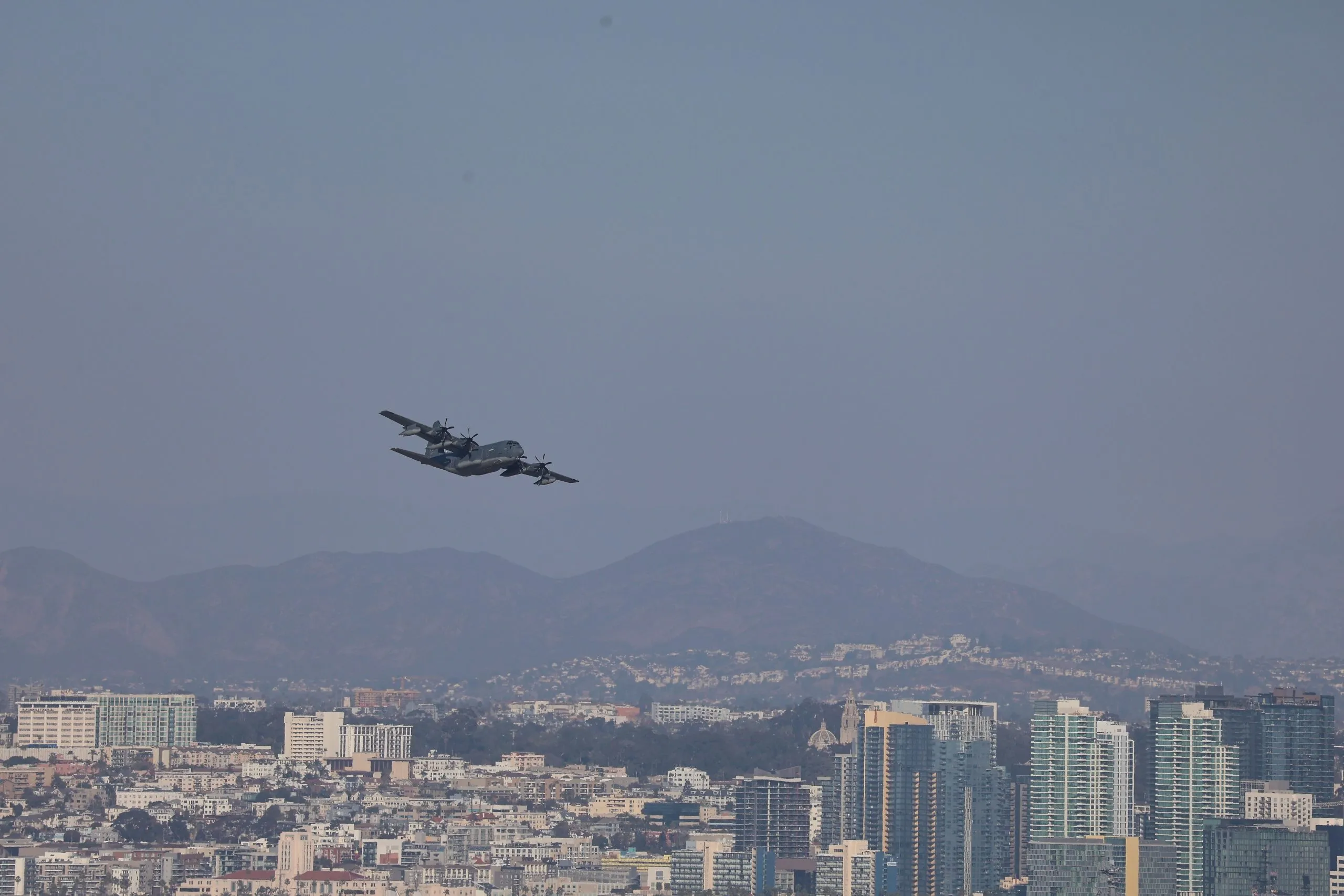 Grey Lockheed C-130 Hercules banking over the San Diego skyline after takeoff from North Island.