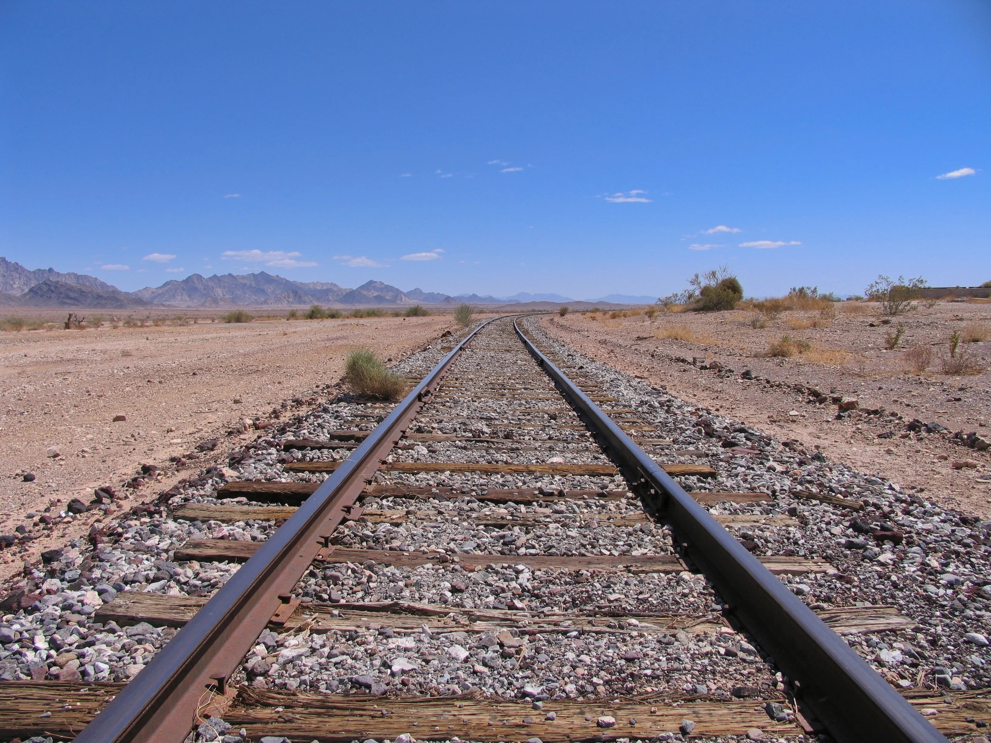 Rusty railroad tracks curving through desert toward distant mountains near Midland, California.