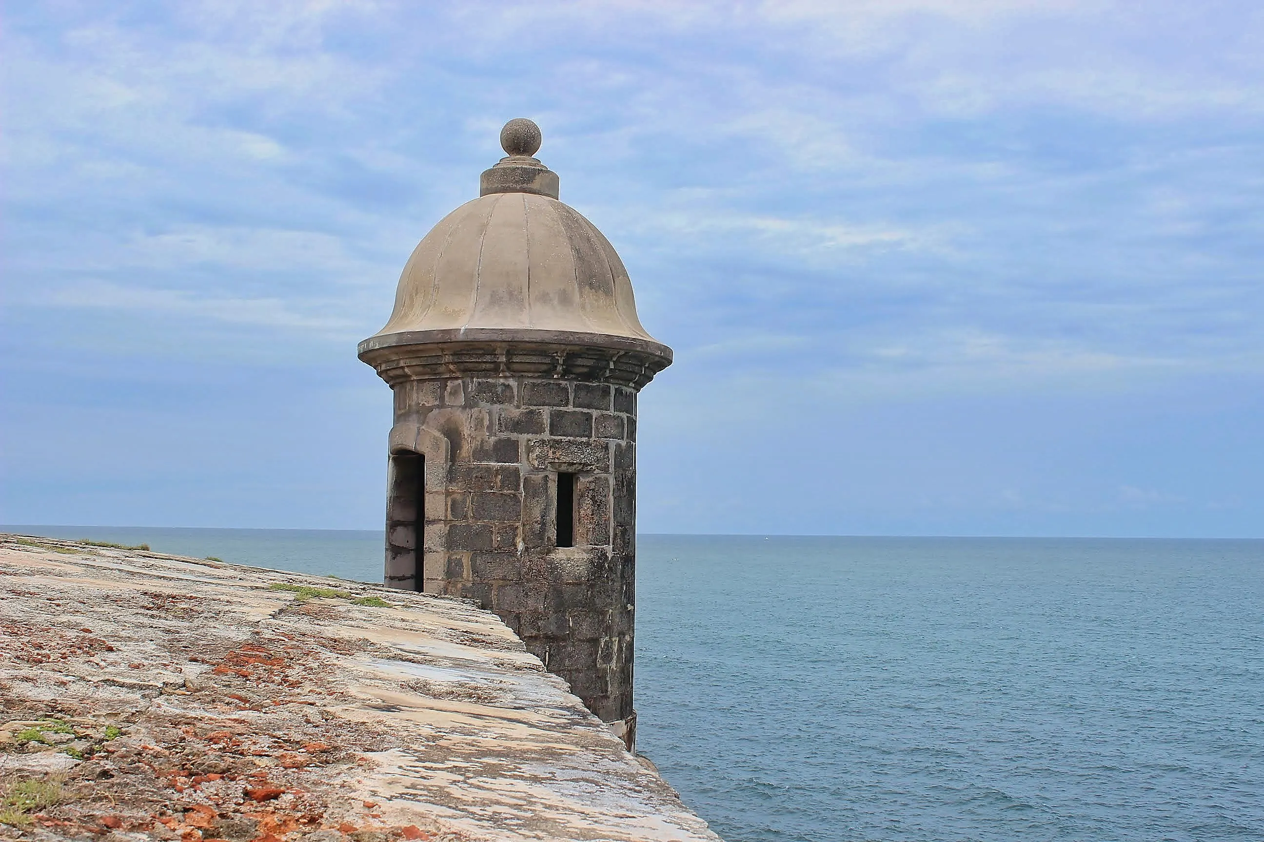 Stone garita perched on El Morro's wall above turquoise Caribbean water.