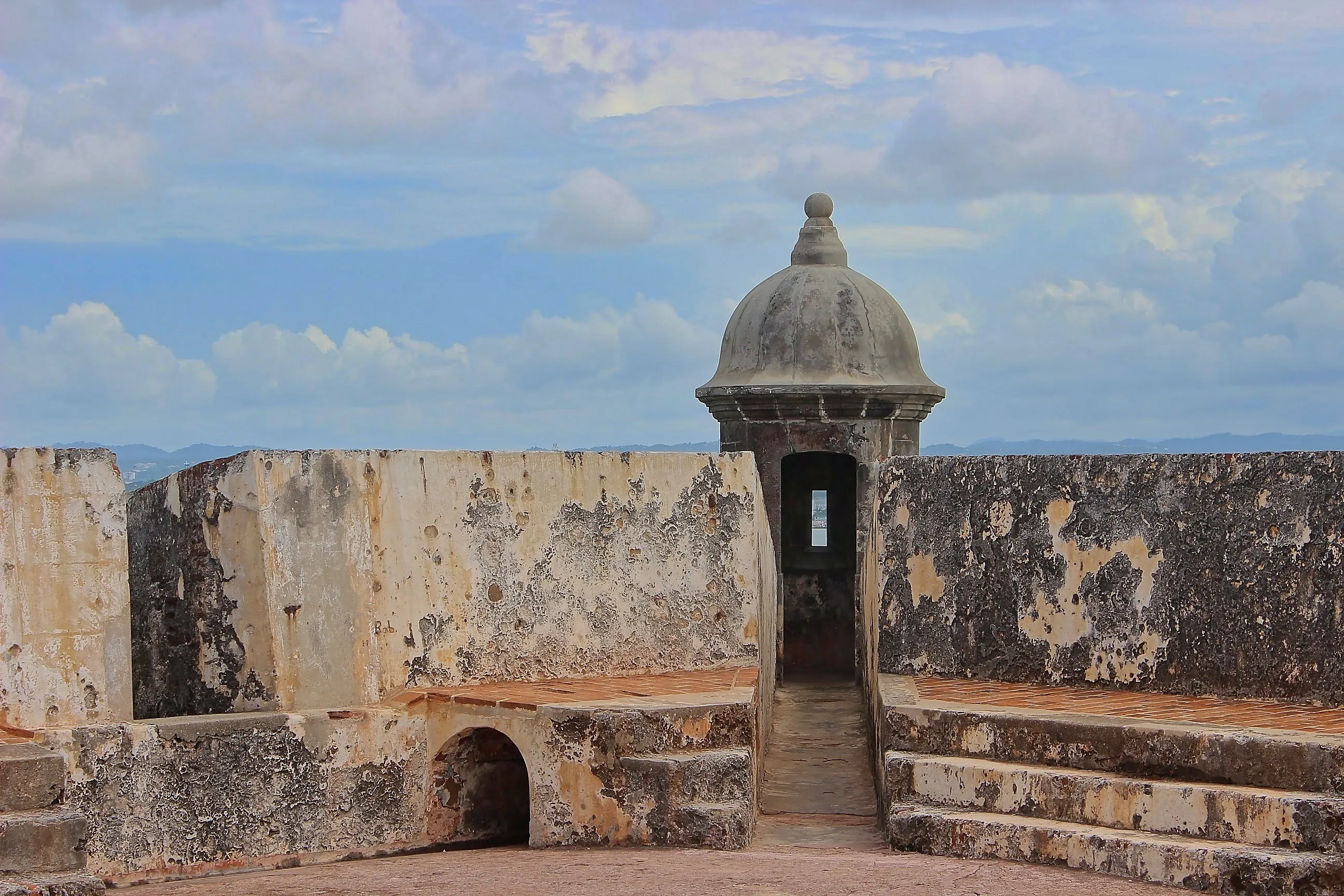 Weathered stone garita at the corner of El Morro's ramparts under cloudy skies.