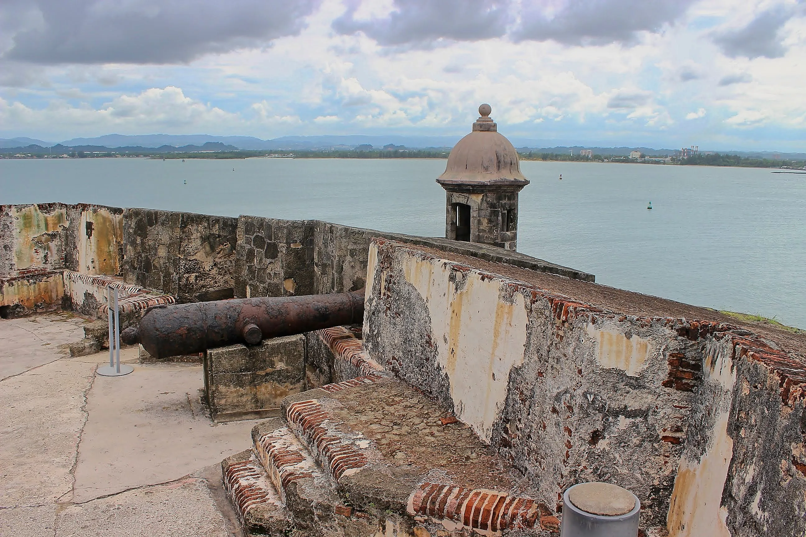 Rusted cannon on El Morro's ramparts beside a garita overlooking the bay.