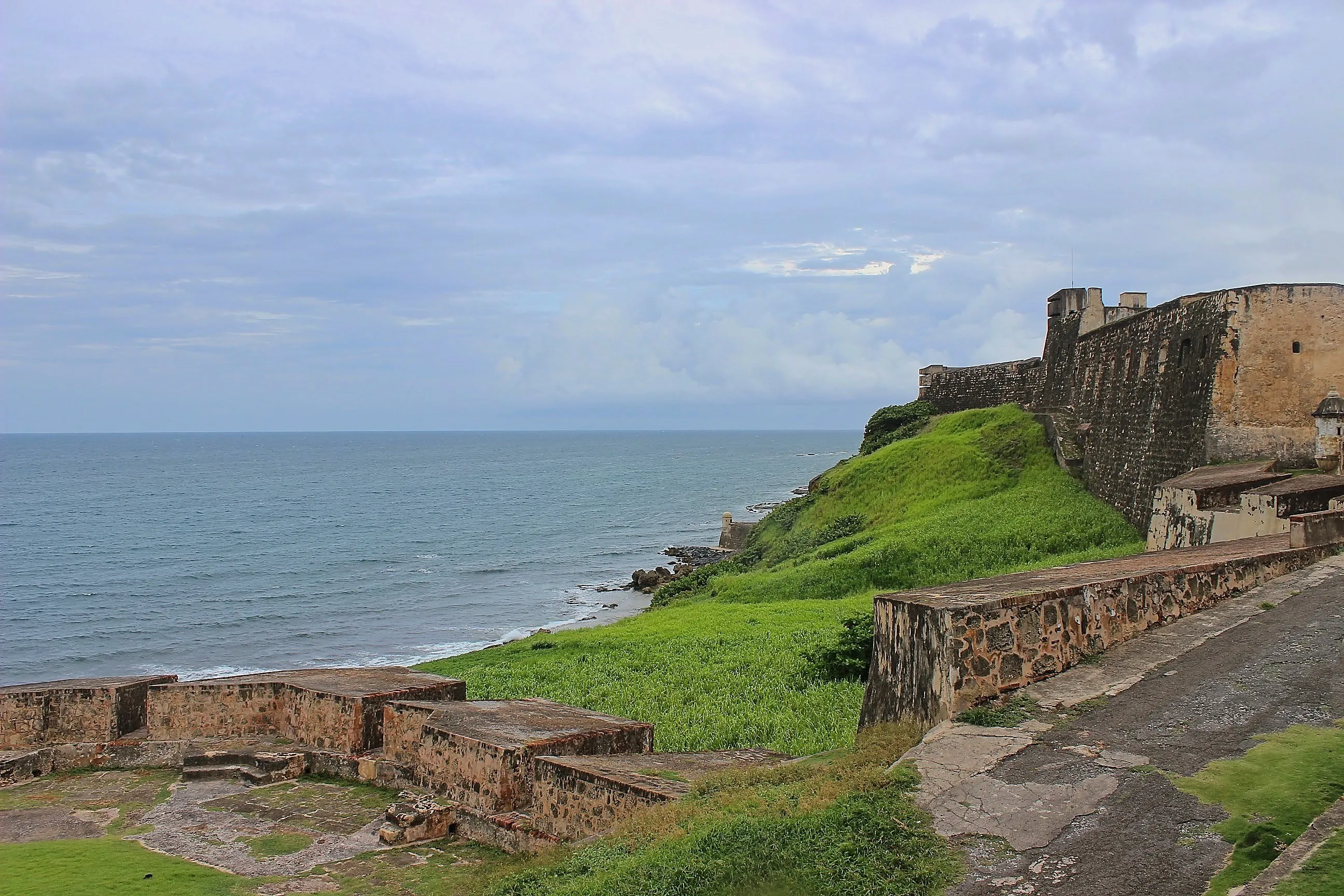 Castillo San Cristóbal walls on a grassy cliff above the rocky Atlantic shore.